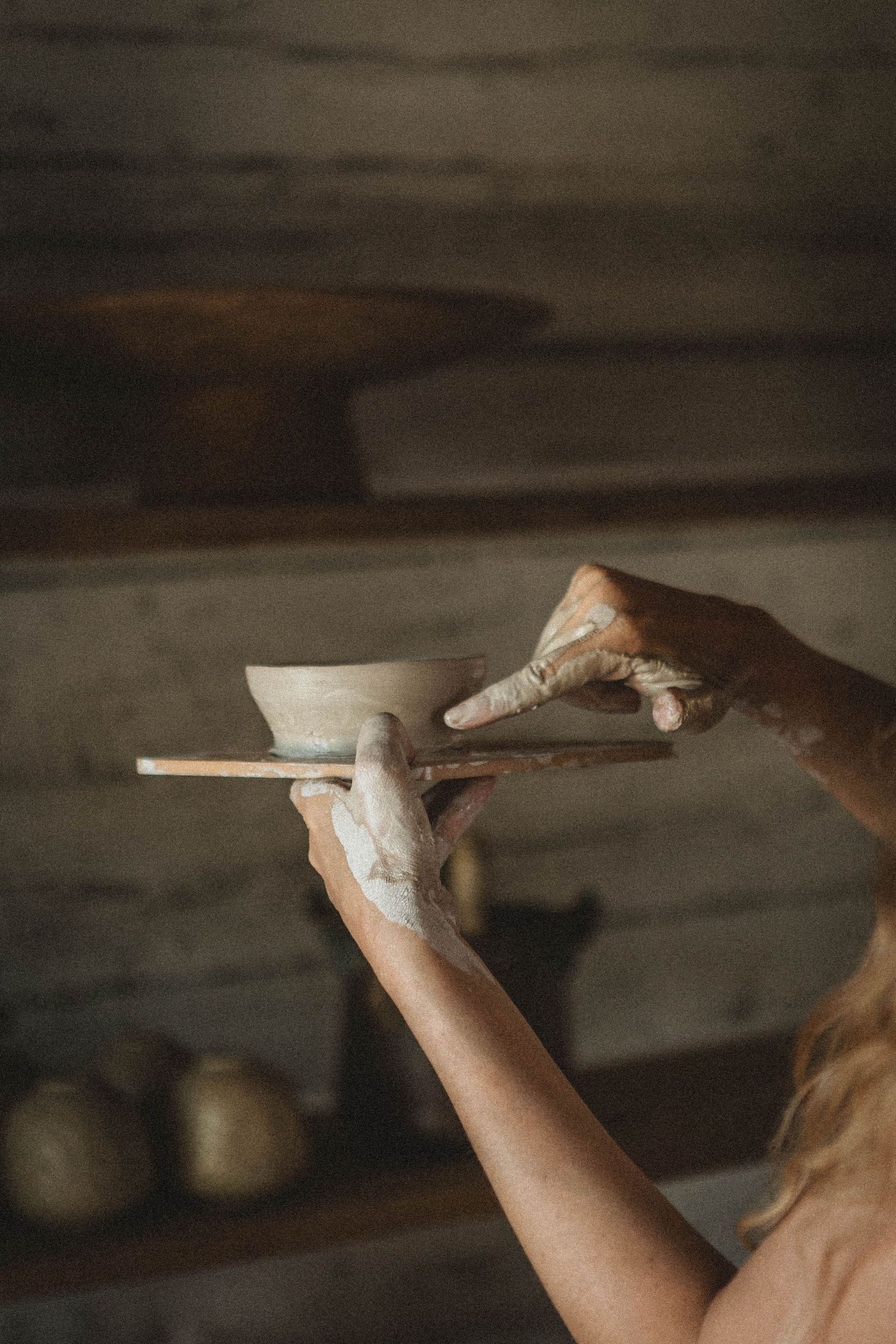 Clay artist's hands carefully trimming a ceramic piece using pottery tools.