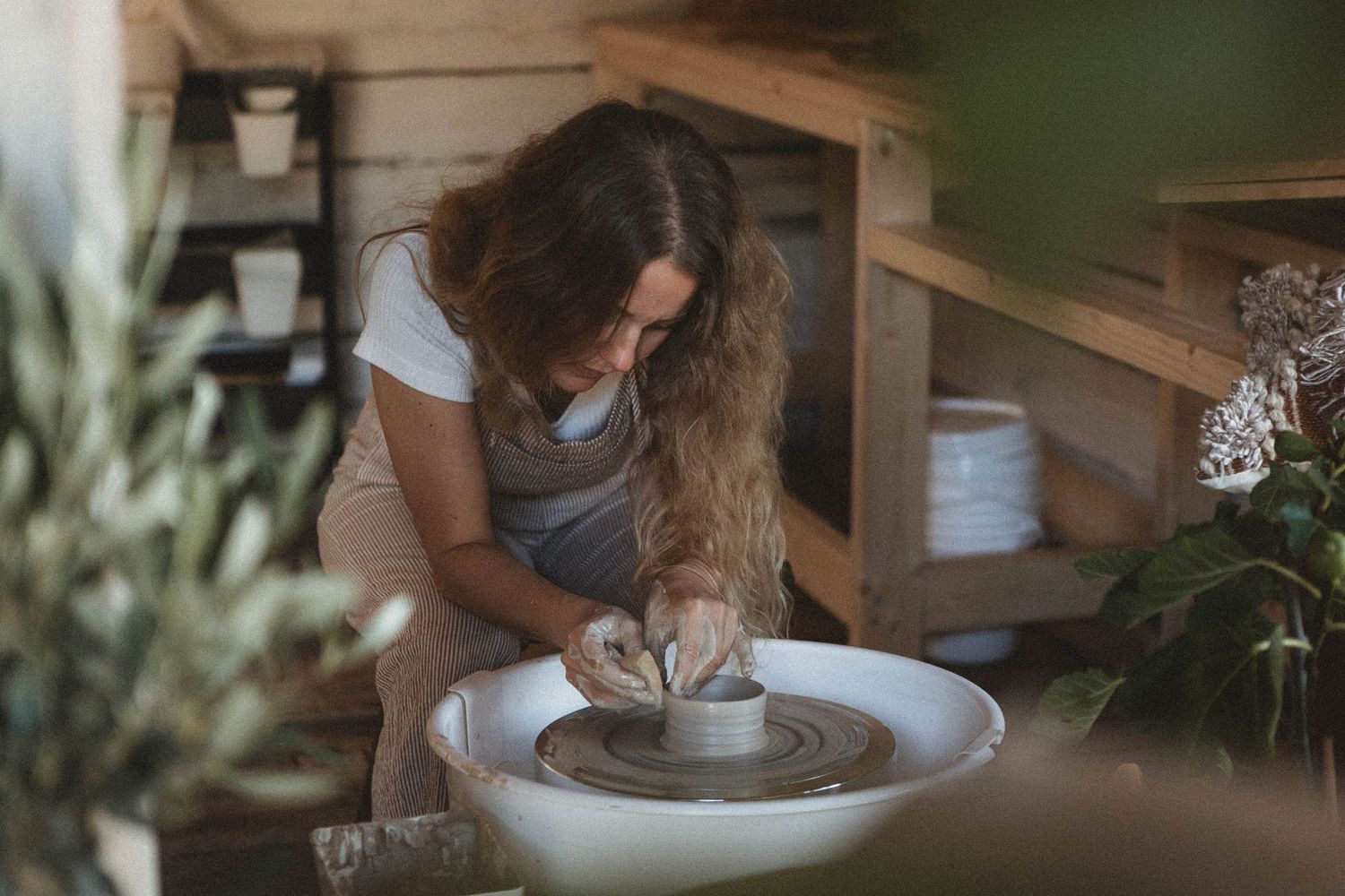 Artist at work in a serene pottery studio surrounded by plants and natural light.