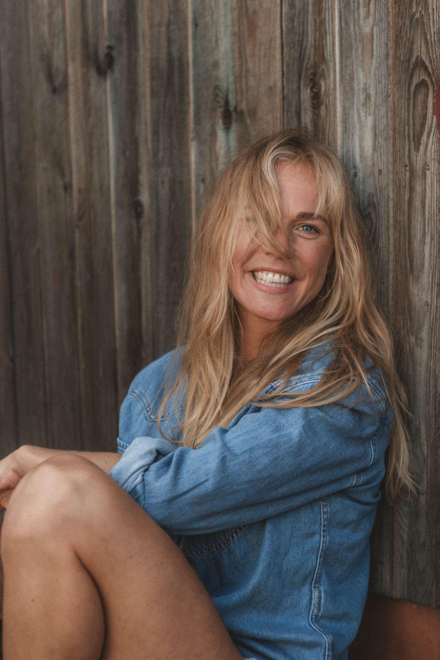 Joyful portrait against rustic wooden wall wearing denim shirt with tousled blonde hair.