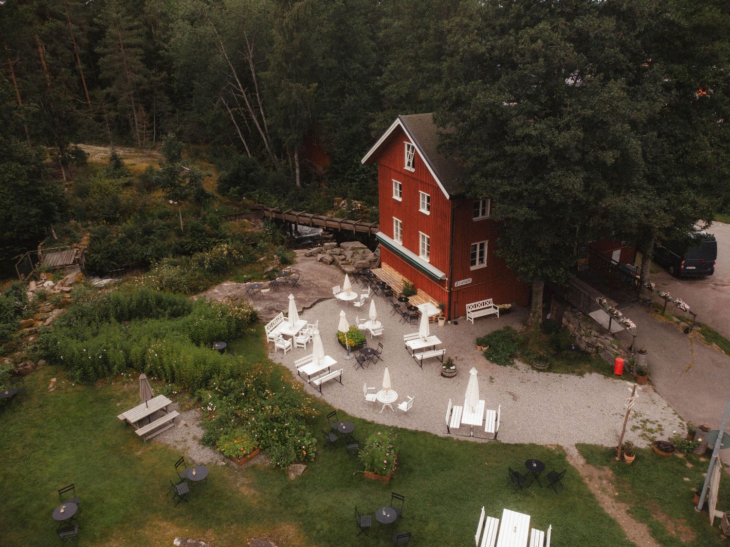 Aerial view of a red wooden house with white patio furniture surrounded by greenery.