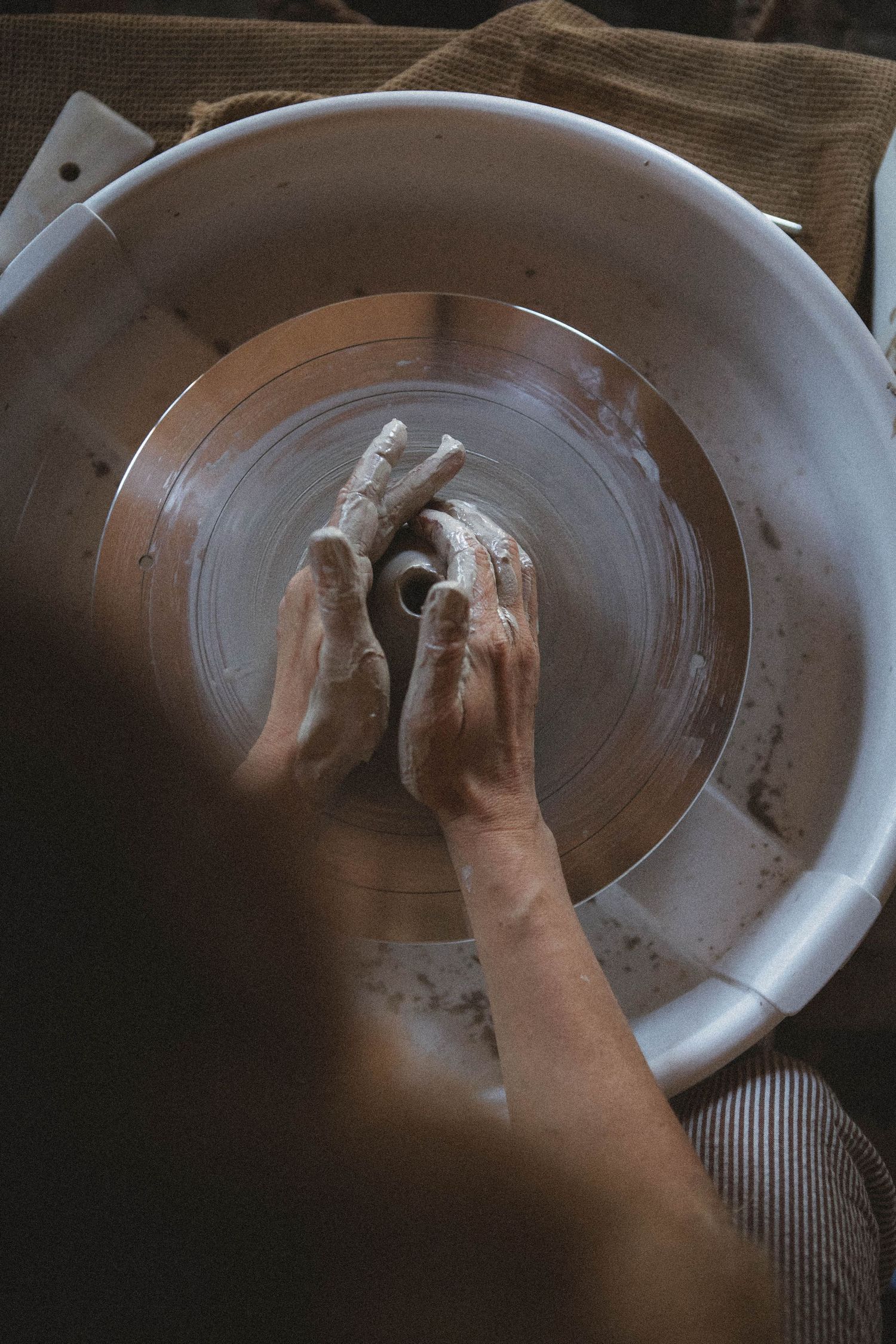 Overhead view of hands shaping clay on a spinning pottery wheel.