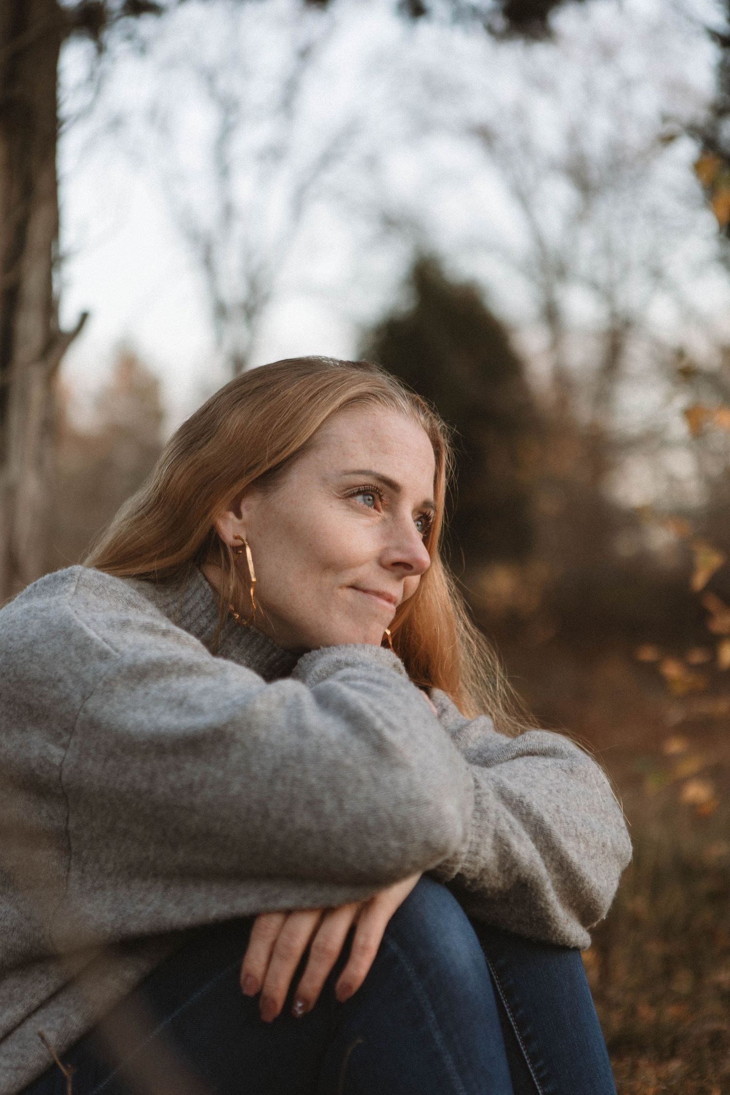 A person in a gray sweater sits thoughtfully outdoors during autumn, gazing into the distance with soft natural lighting.