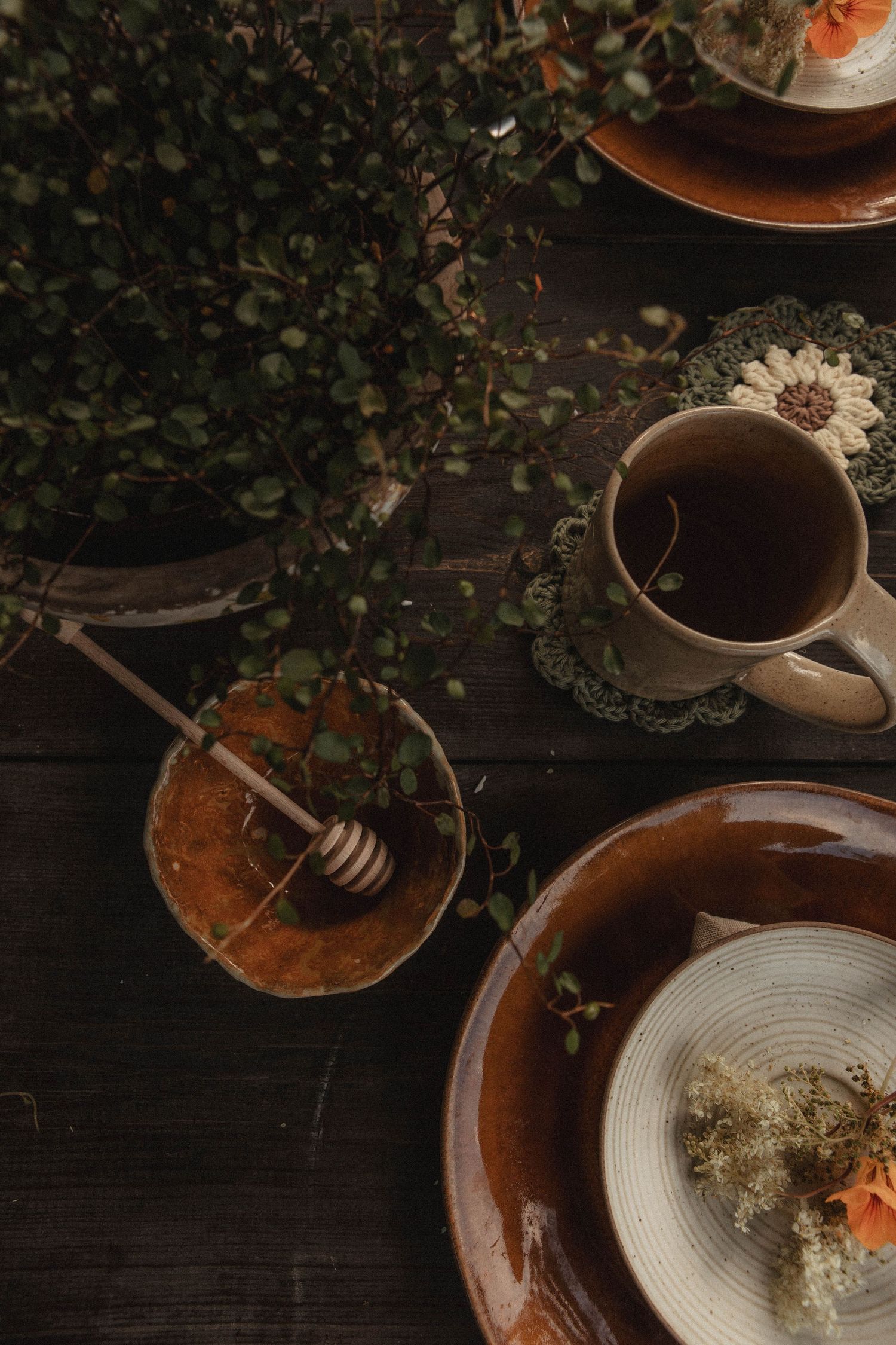A cozy tea setting with honey pot and rustic plates on a dark wooden table.