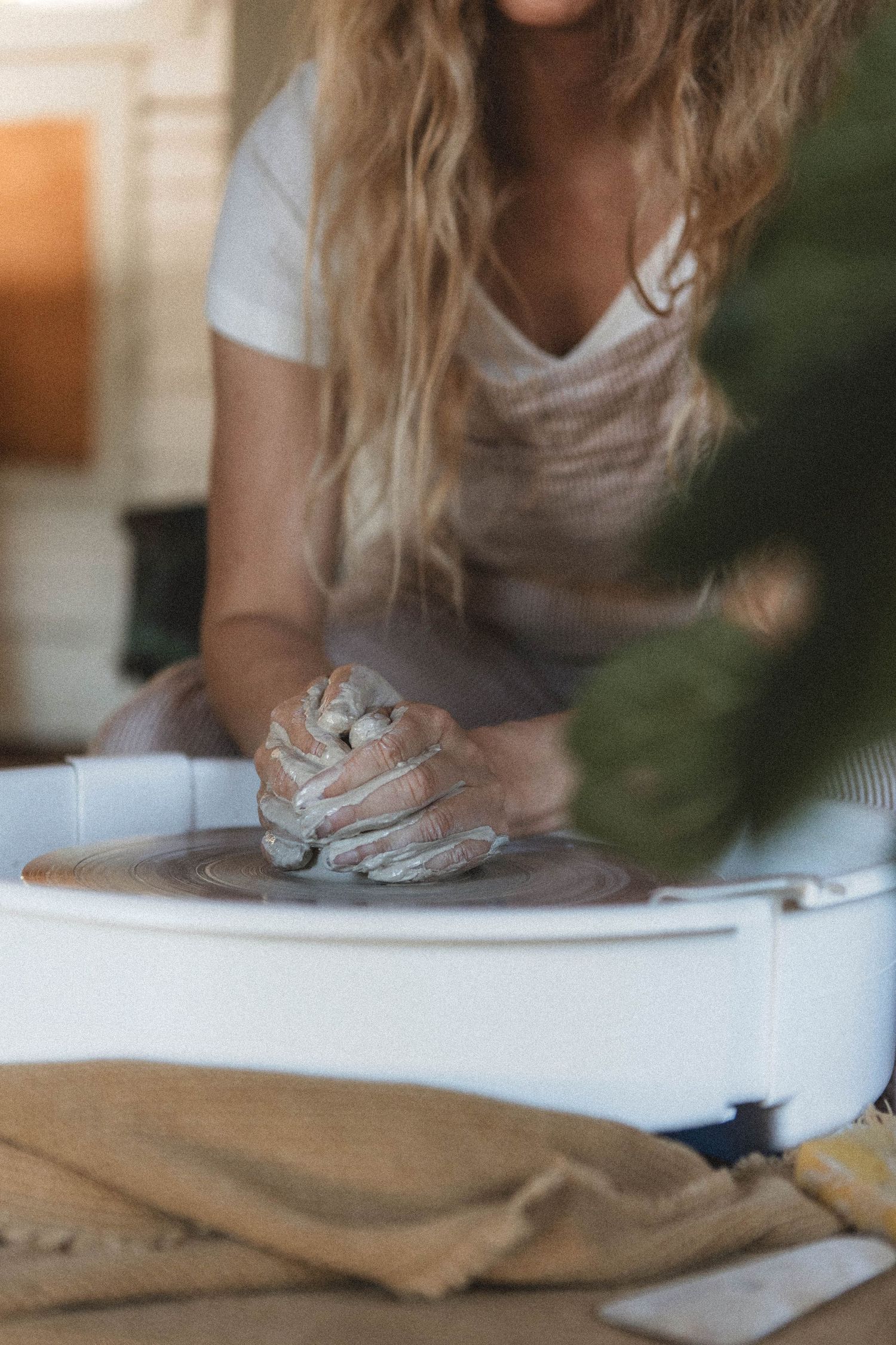 Hands work with clay on a pottery wheel in a sunlit studio space.