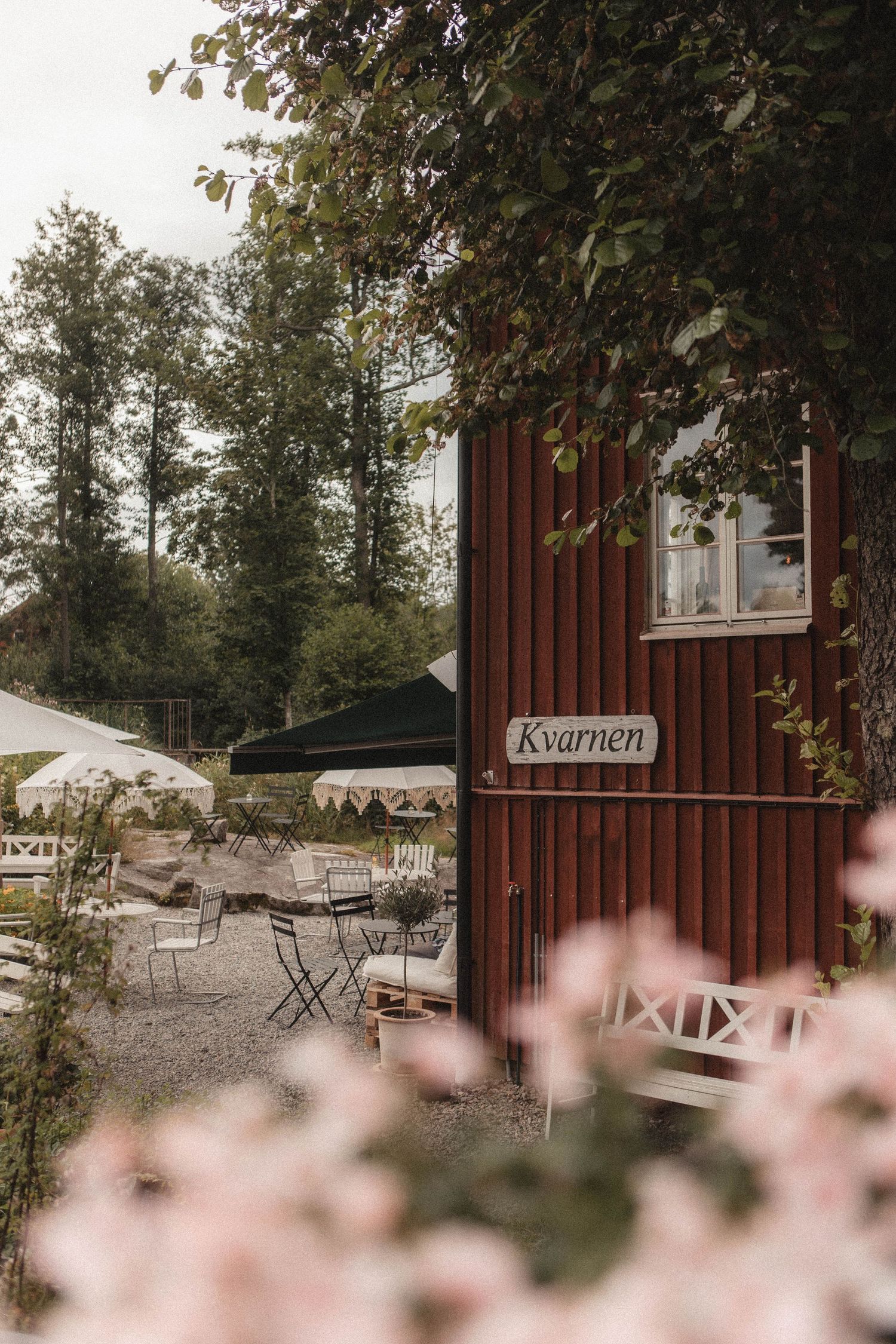 Red wooden cafe building with outdoor seating and pink flowers in the foreground.