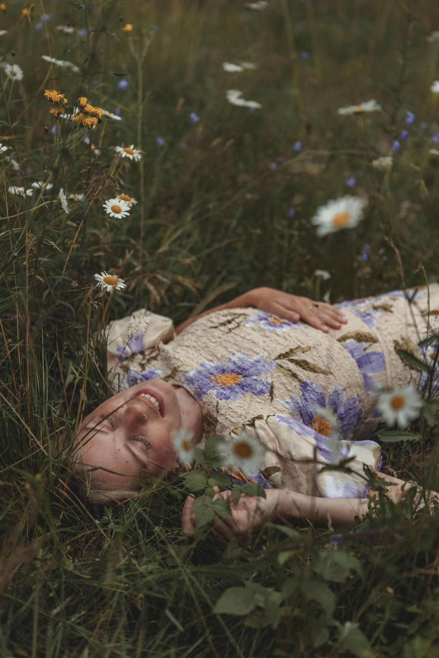A person lies in a meadow of wildflowers wearing a floral dress.
