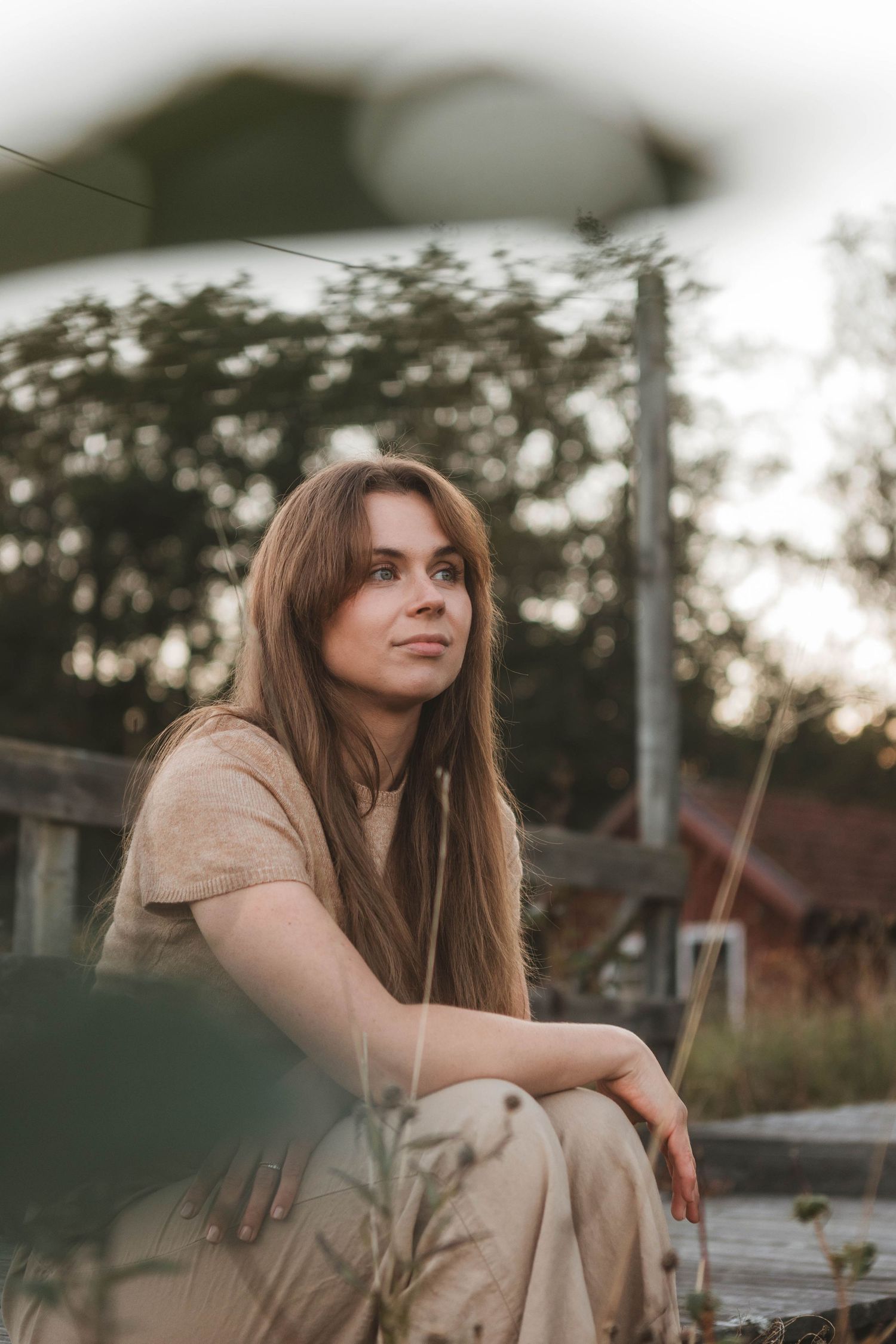 Person in beige outfit sitting thoughtfully outdoors during golden hour.
