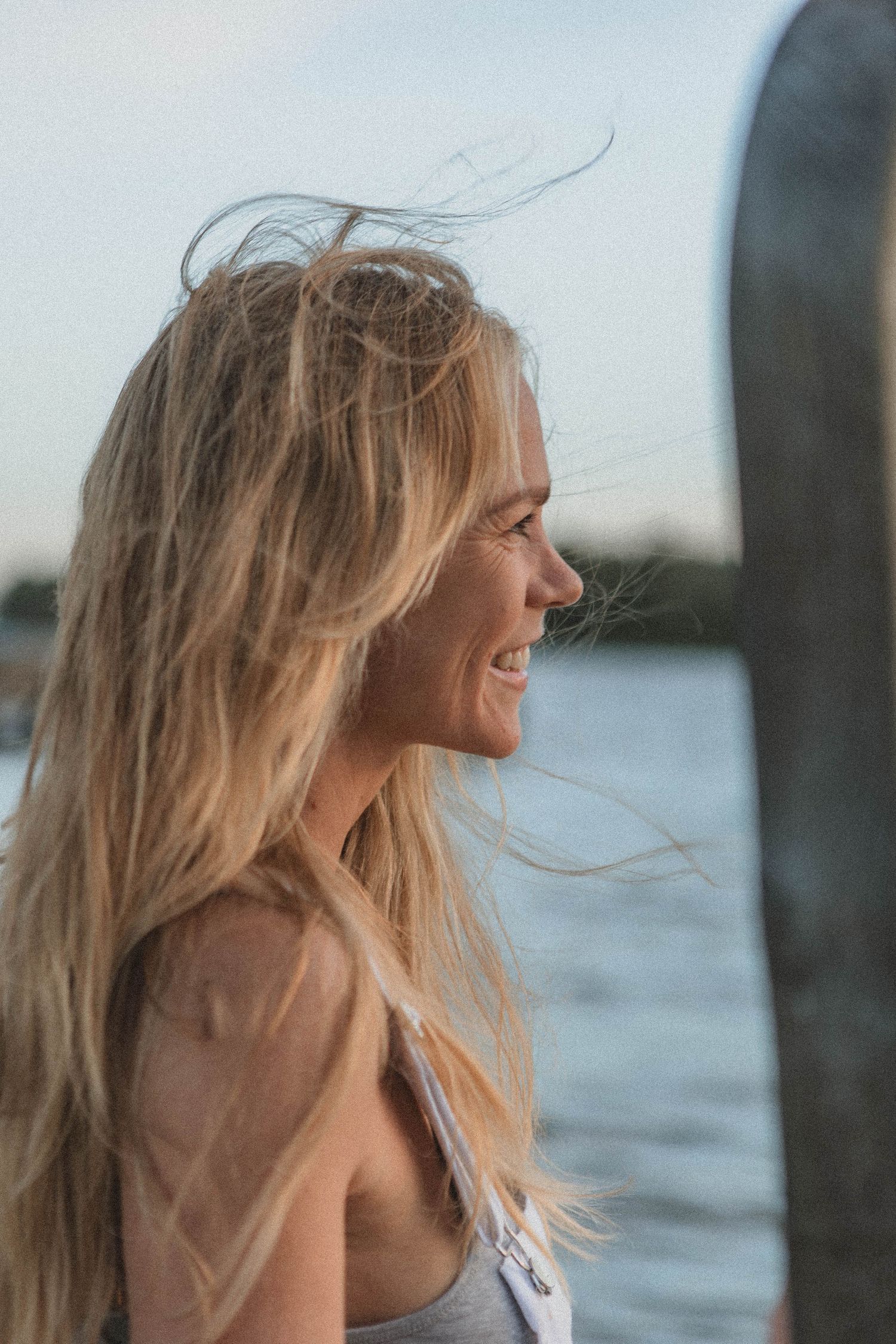 Profile portrait with windswept hair against a waterfront backdrop at golden hour.