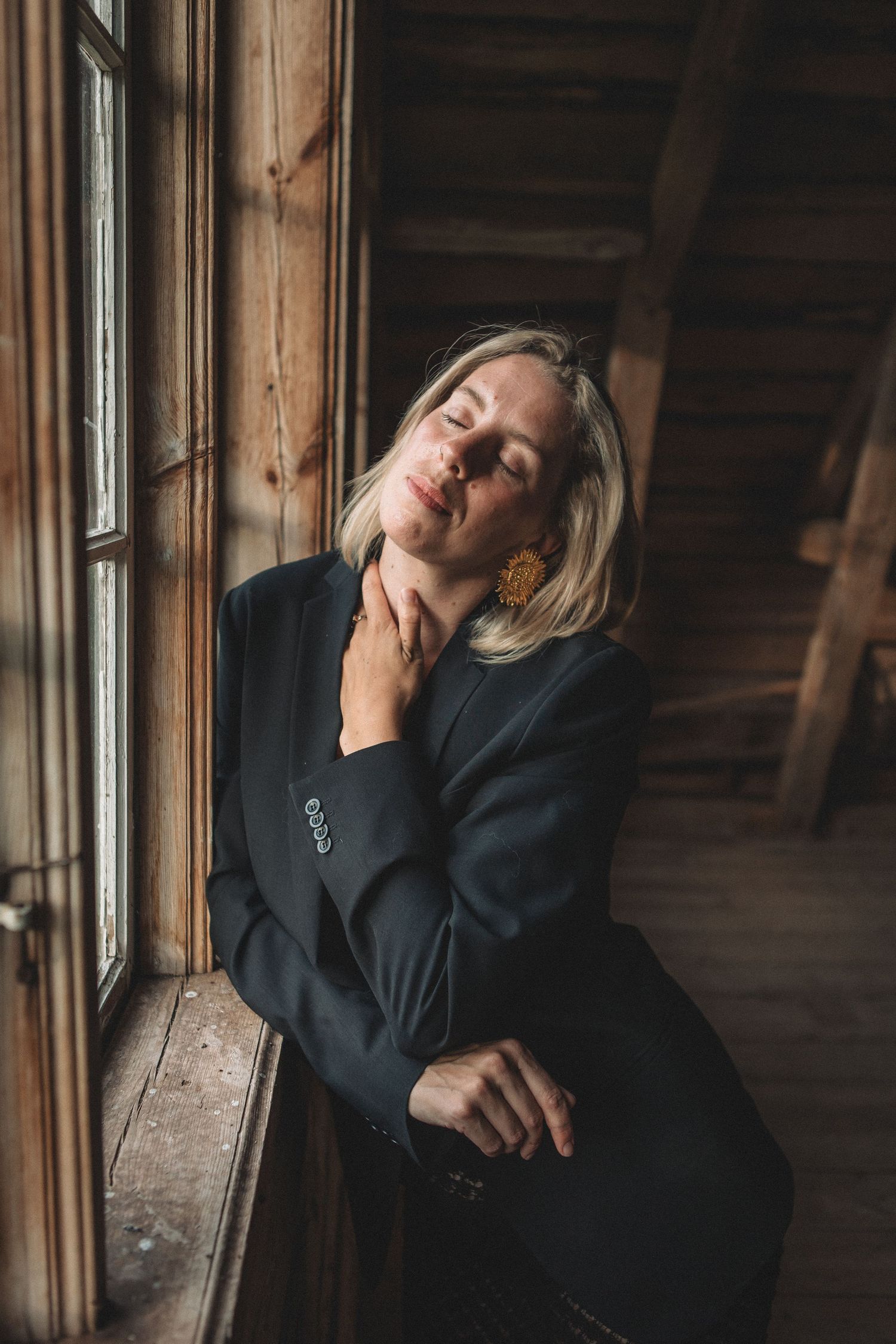 Artistic portrait near window with dramatic lighting in rustic wooden interior.
