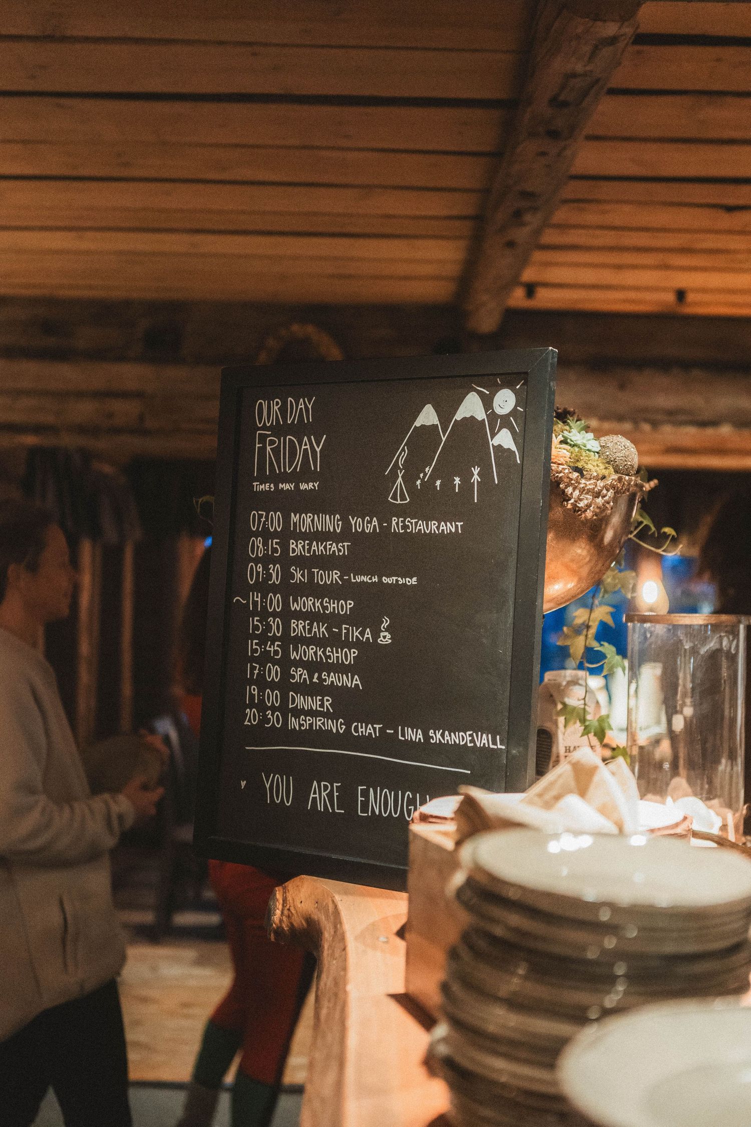 A chalkboard menu featuring daily activities and mountain illustrations in a wooden cabin setting.