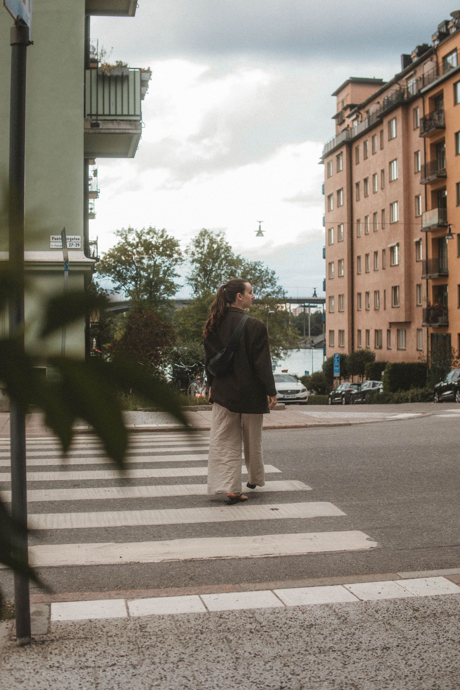 Person in dark jacket crossing a zebra crossing on a cloudy day in a residential area with apartment buildings.