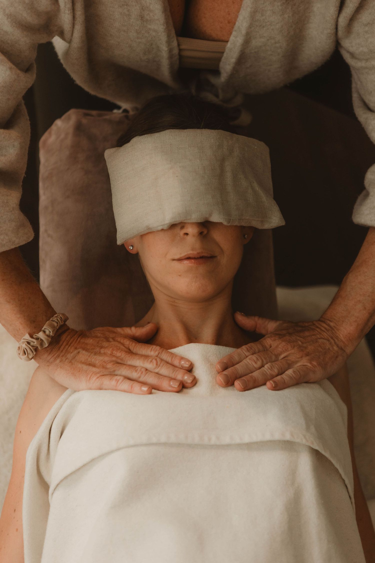 A person receiving a relaxing spa treatment with a cloth covering their eyes and hands massaging their shoulders.
