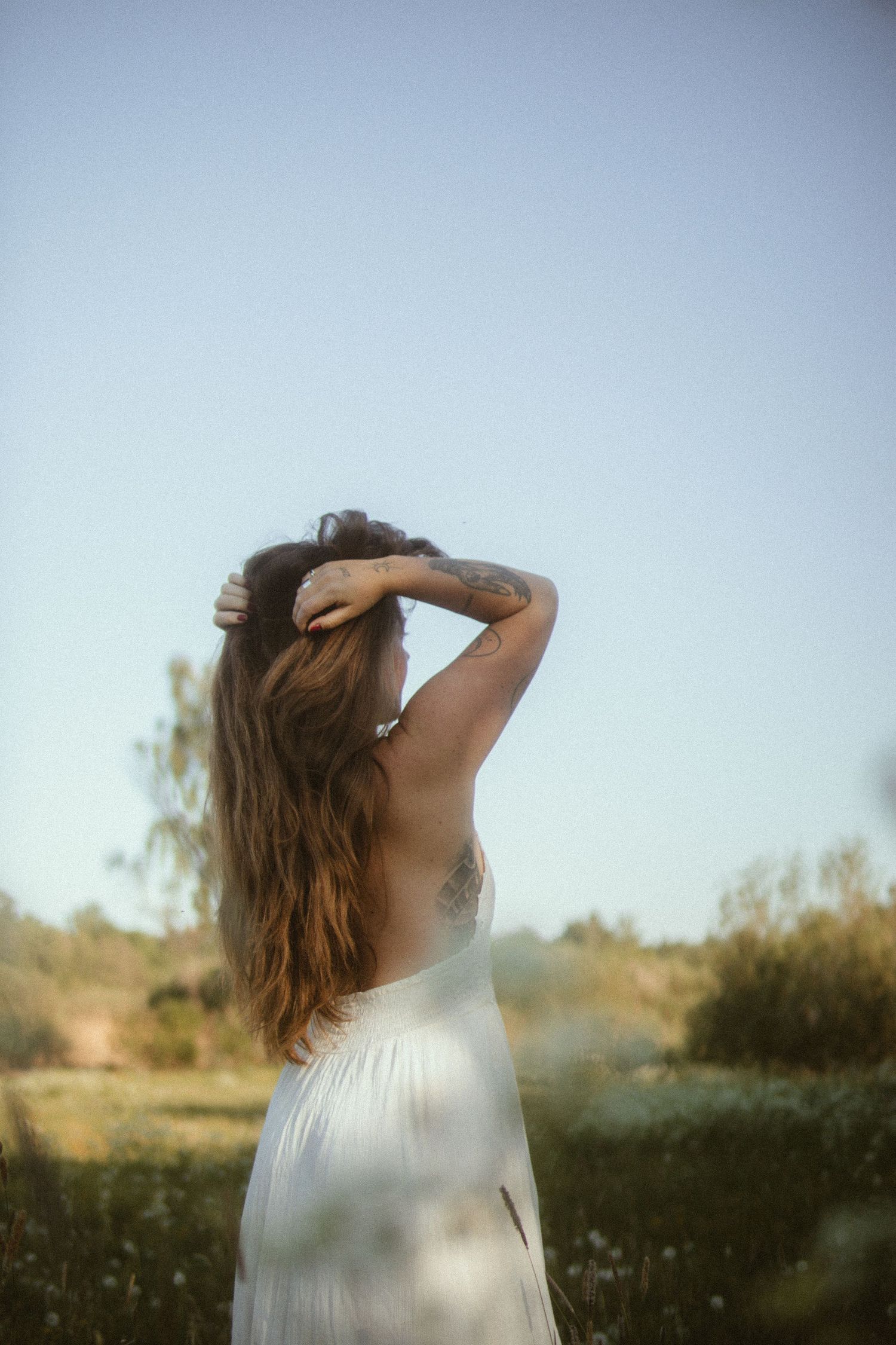 Ethereal portrait of someone in a white dress standing in a field during sunset.