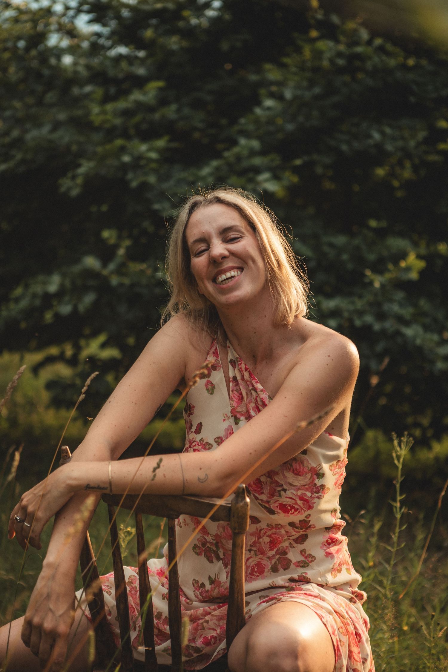 A summer portrait of a person in a floral dress sitting outdoors with natural backlighting and foliage.