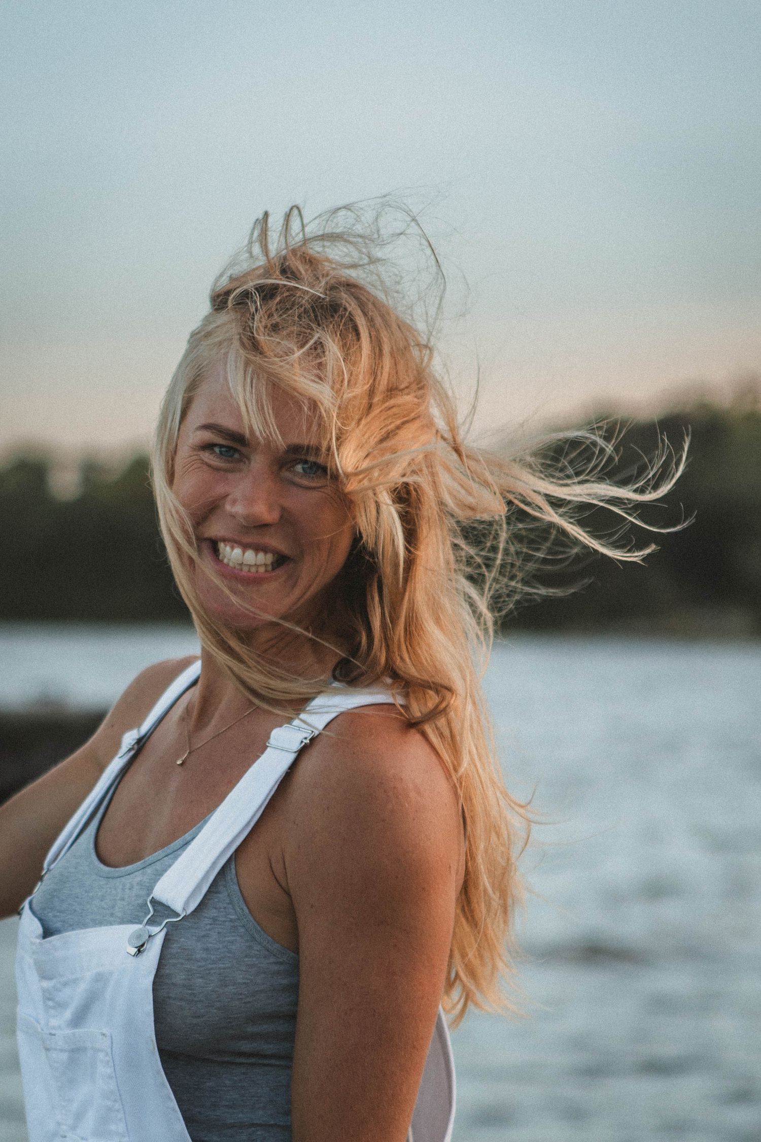Windswept portrait in white overalls against a waterfront sunset background.