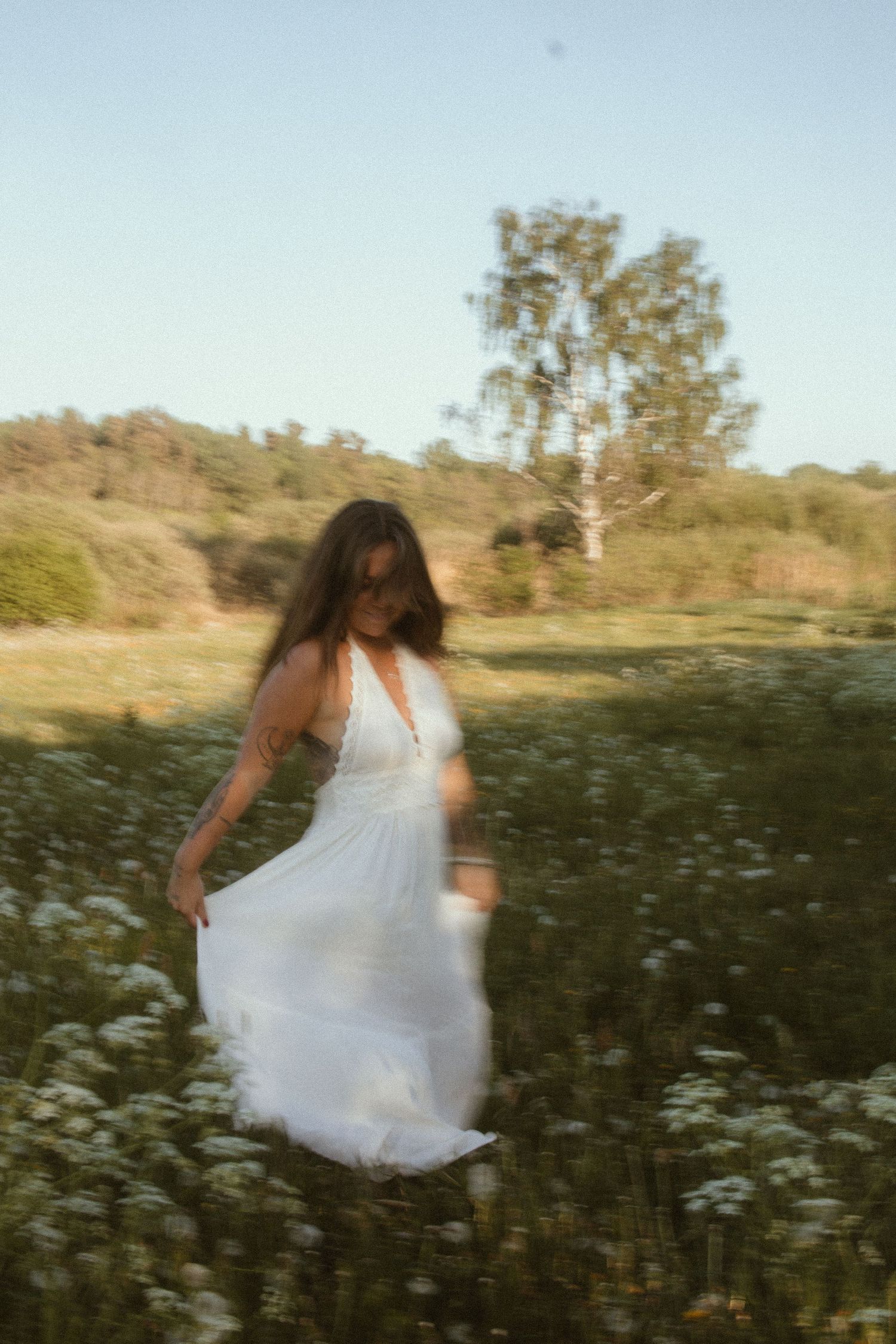 A blurred motion shot captures dancing movement in a white dress among wild daisies at sunset.