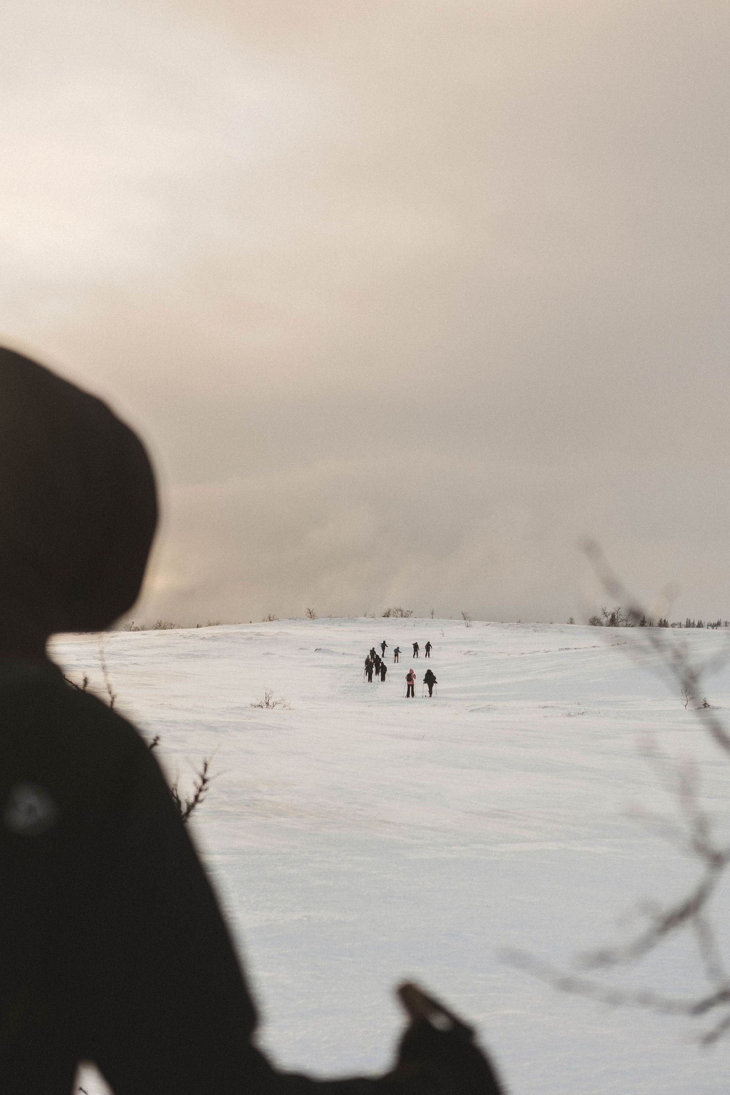 A silhouetted view of people walking across a snowy winter landscape in the distance.