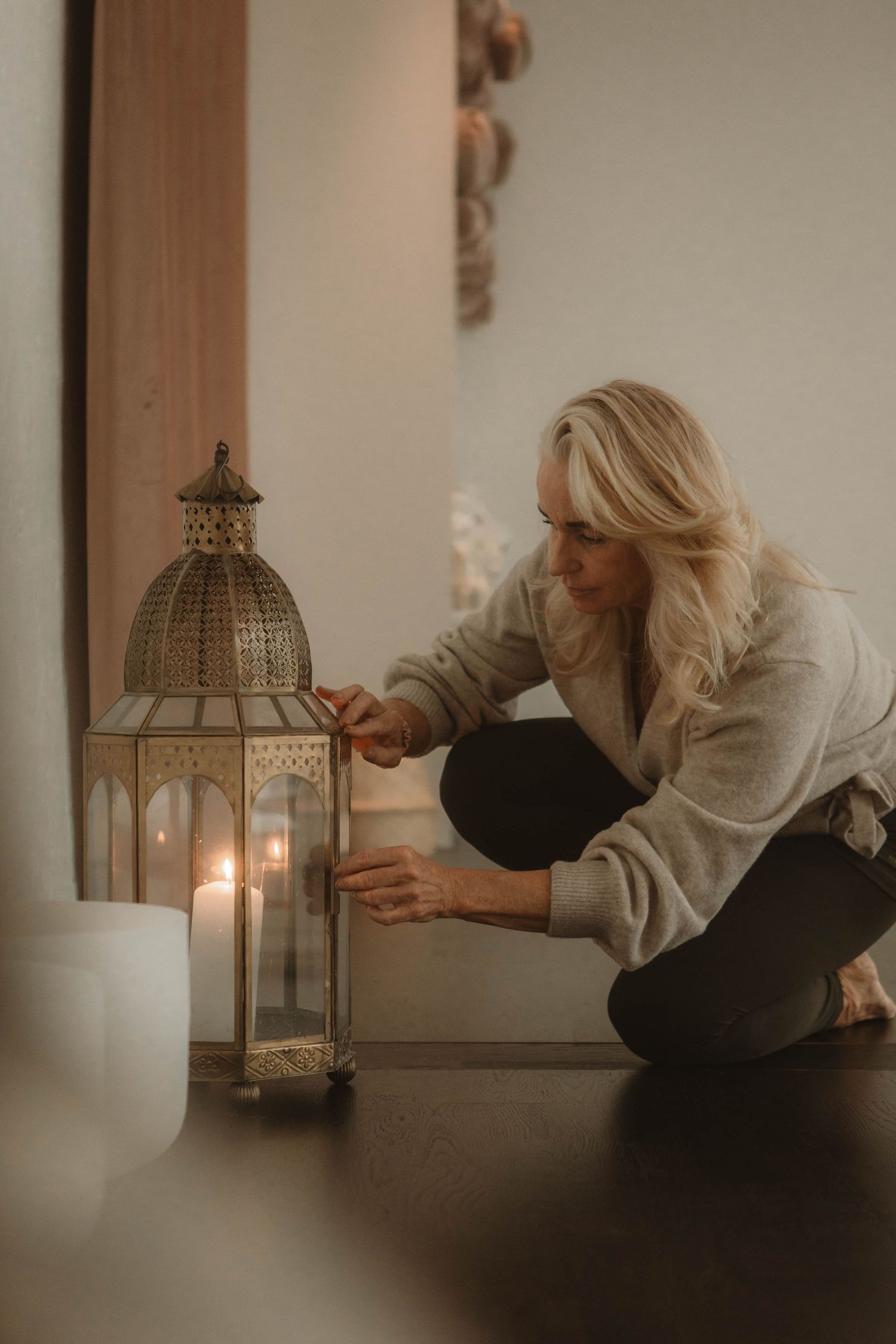 Person in cozy sweater lights a decorative metal lantern on dark floor in moody atmospheric setting.