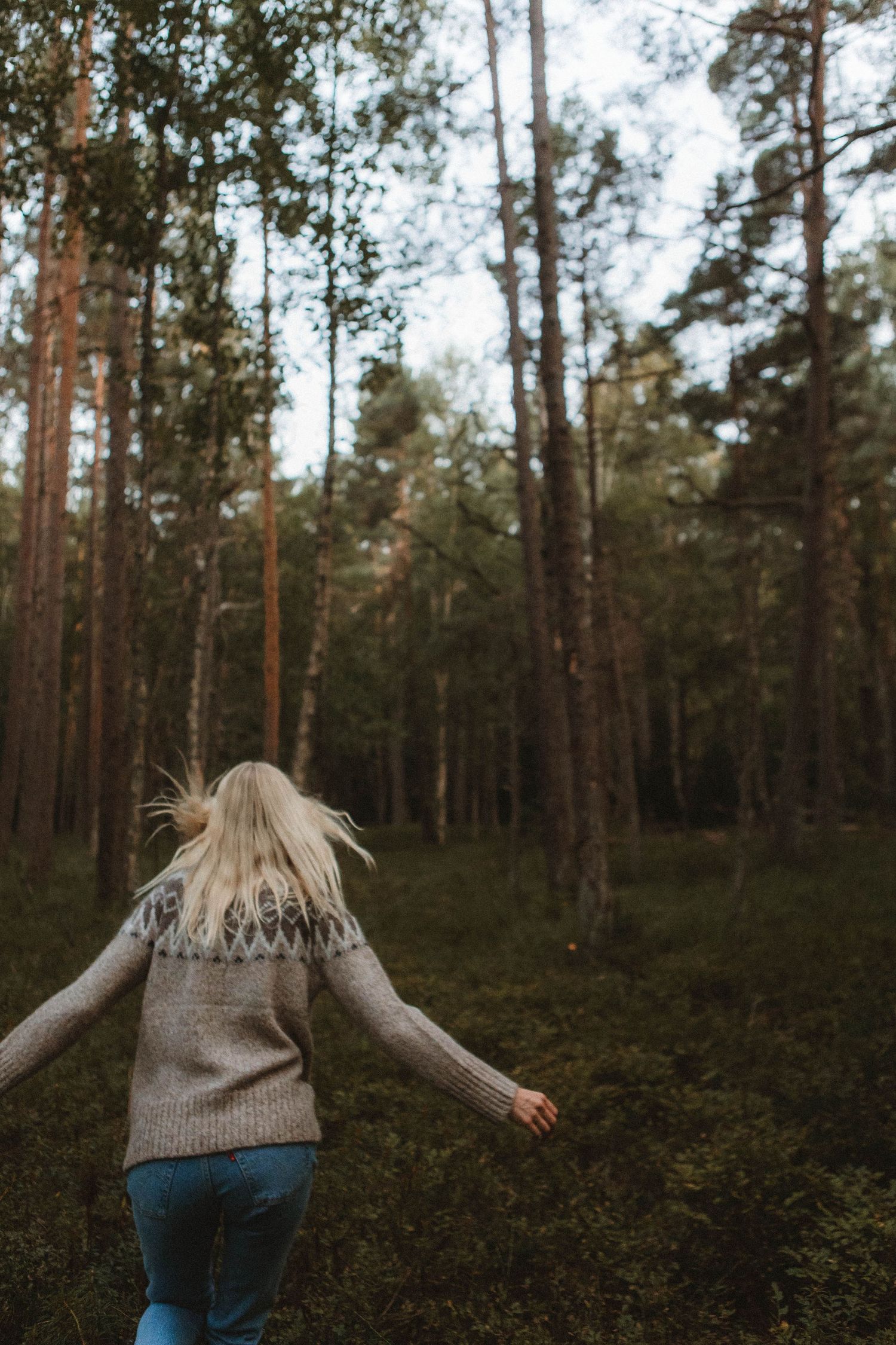 Person in patterned sweater spins playfully in a serene forest setting.