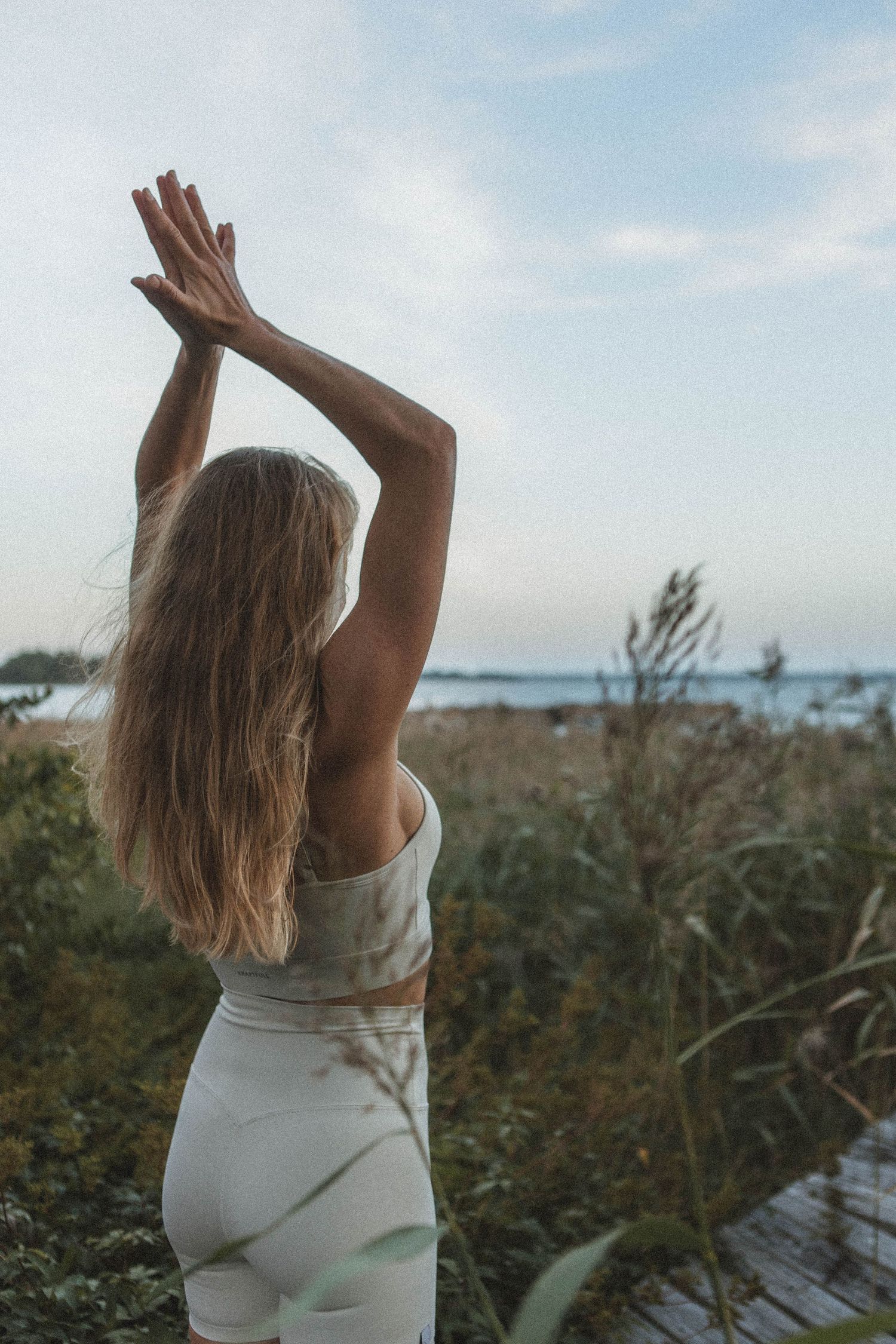 Silhouette of person in white outfit raising arms toward ocean horizon.