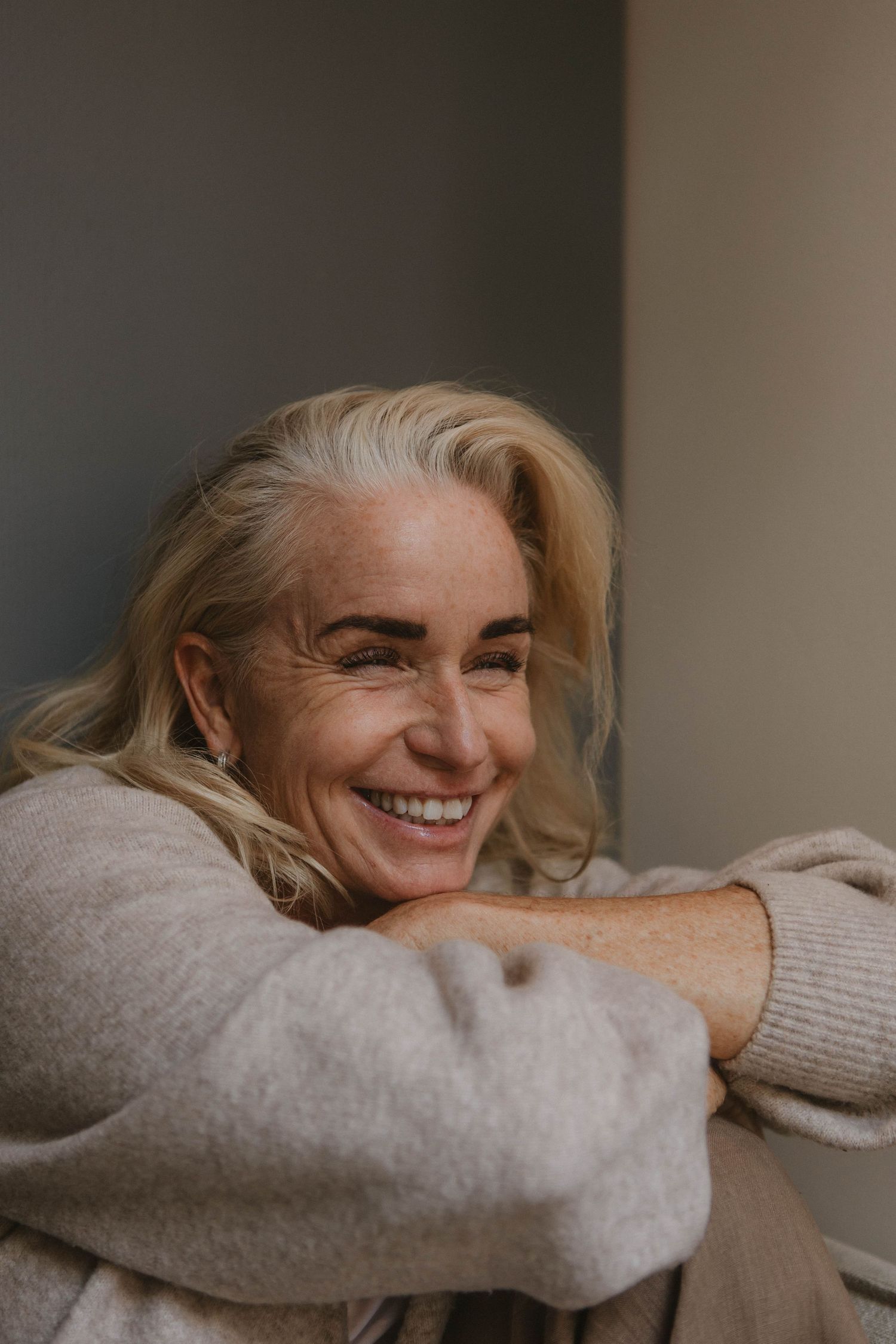 Casual portrait featuring bright smile and cozy sweater in moody lighting.