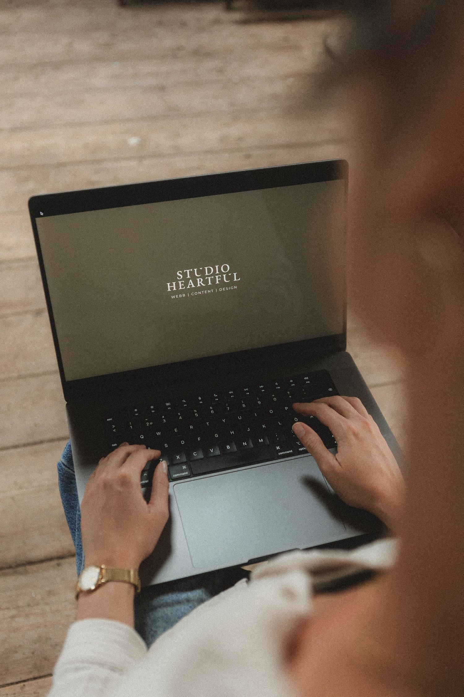 Person typing on a sleek black keyboard on a wooden desk surface in moody lighting.