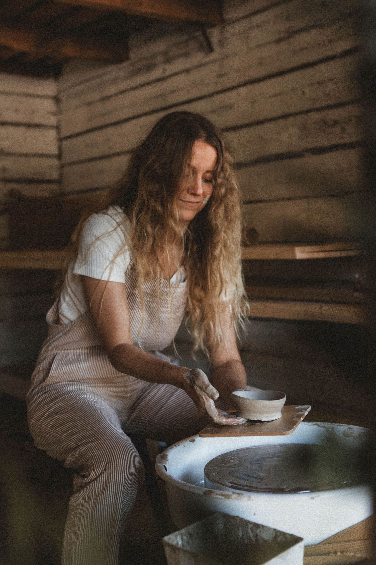 Potter working on clay vessels in a cozy wooden studio with natural lighting.