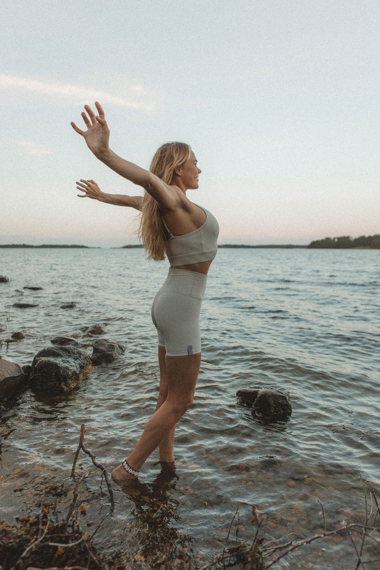 Free-spirited pose by rocky shoreline in white activewear at sunset.