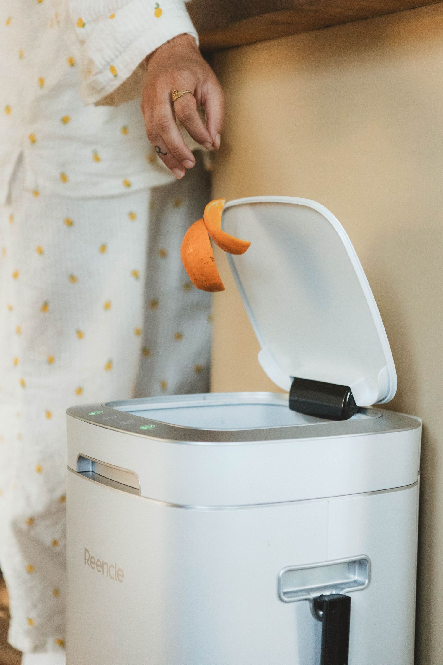 Demonstration of hands placing orange peels into a white smart garbage bin with automated lid.