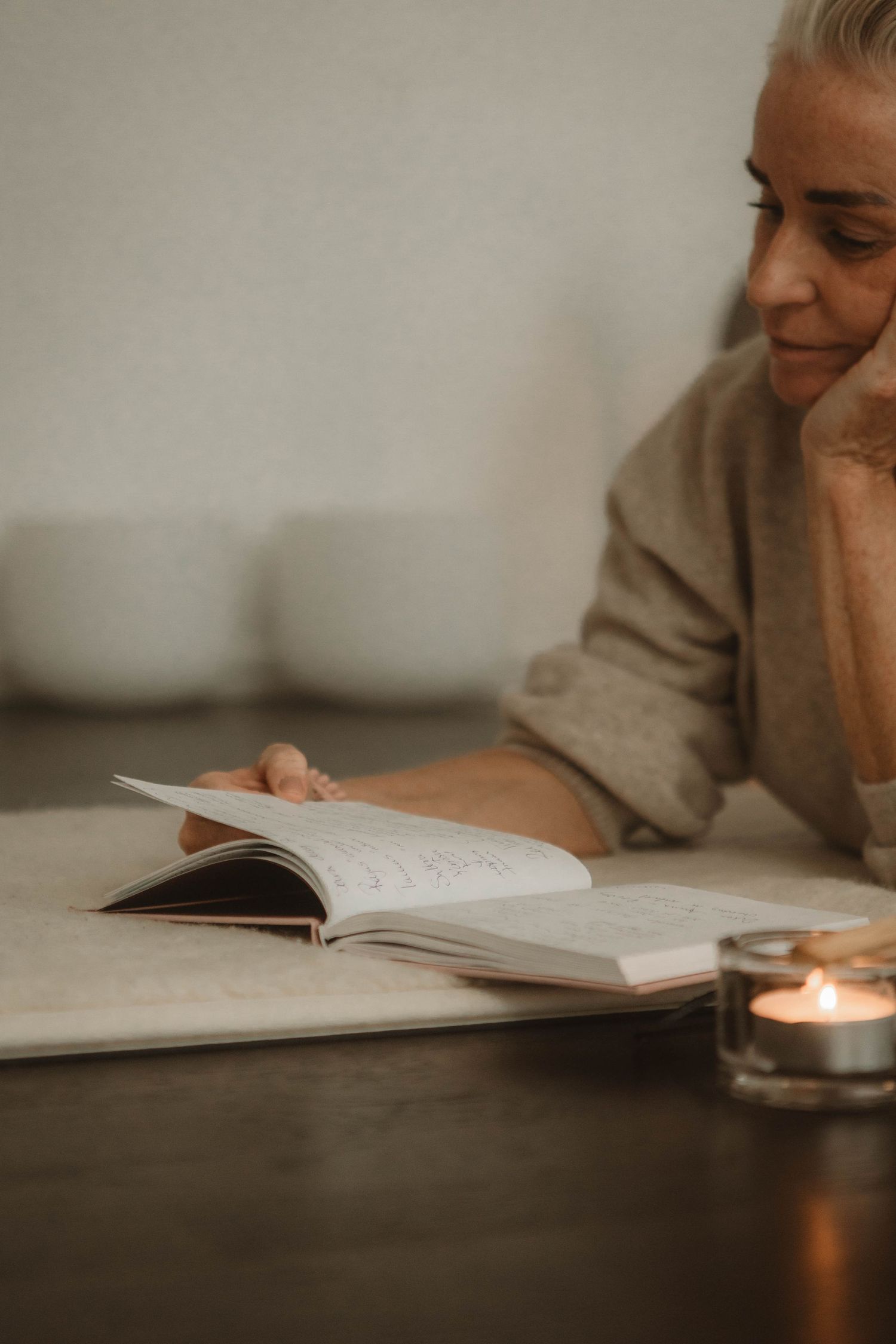 A person reads a book by candlelight in a cozy setting with warm lighting and soft tones.