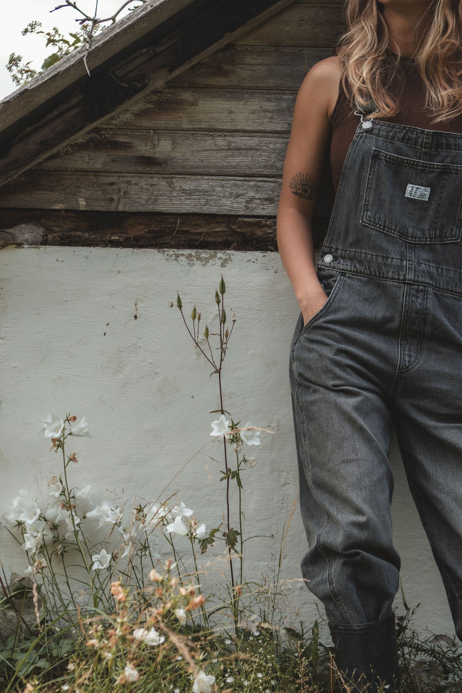Denim overalls against weathered wall with white flowers growing below.