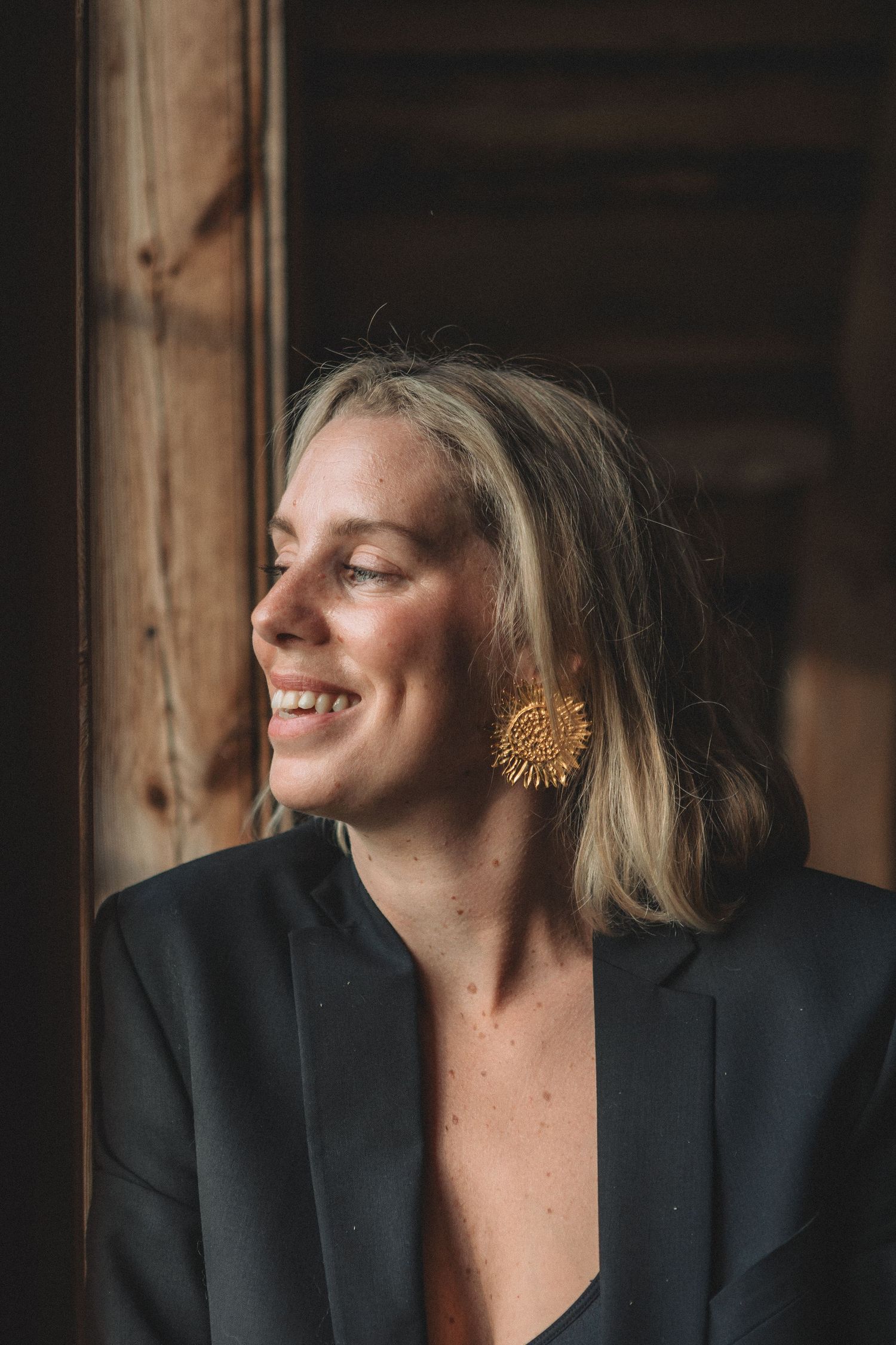 Candid portrait featuring statement gold earring and black blazer in warm lighting.