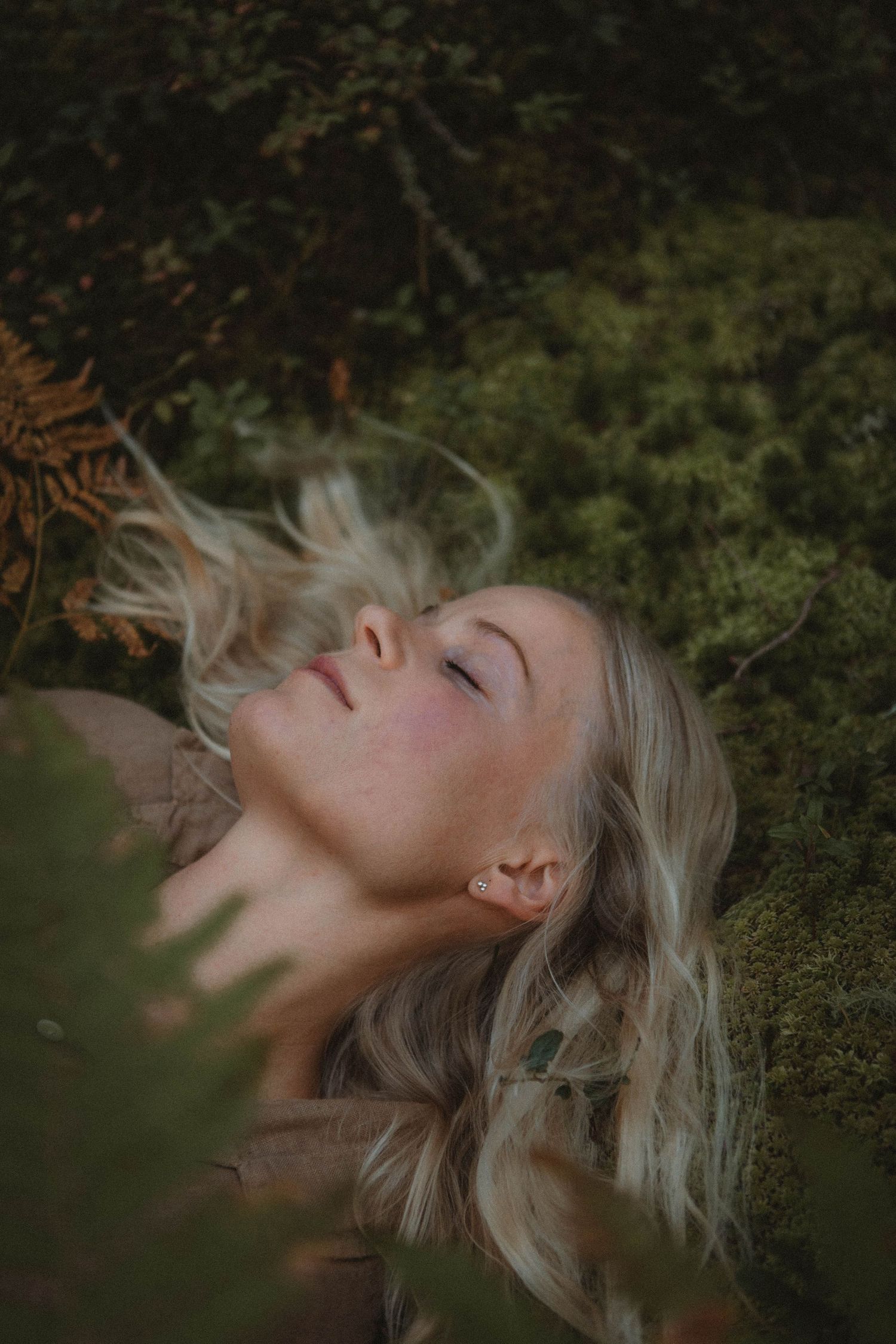 Dreamy forest portrait showing light hair flowing against mossy ground.