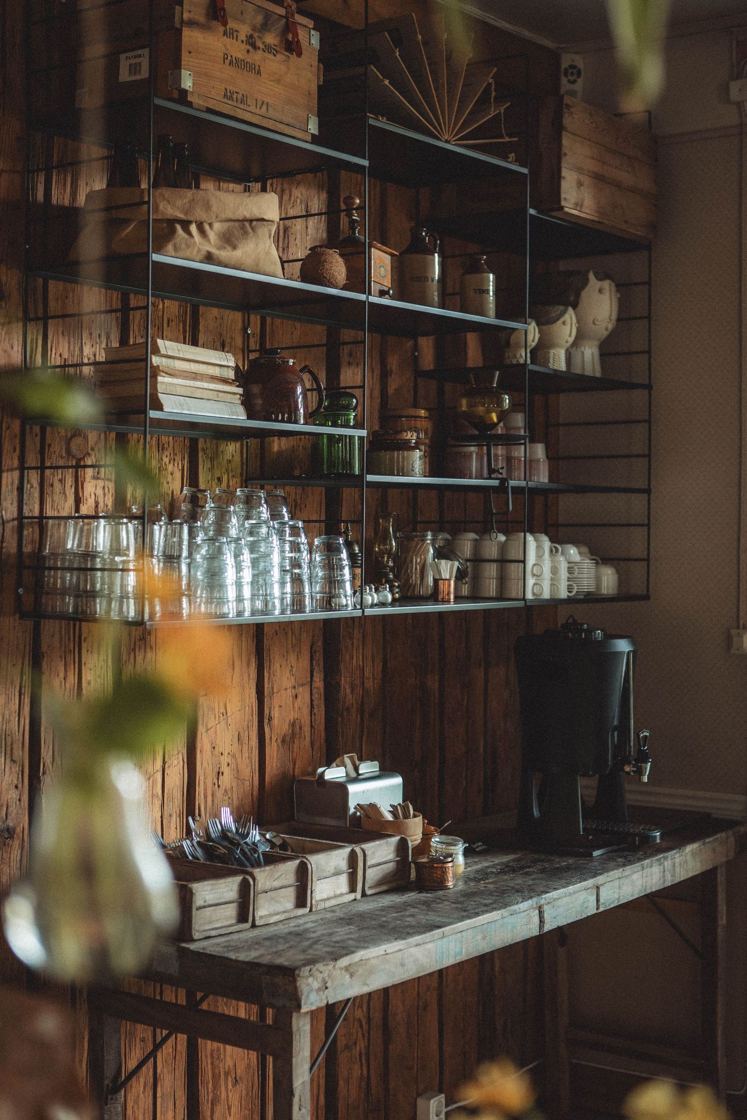 Rustic wooden shelving unit displaying glassware, bottles and vintage decor in a bar setting.