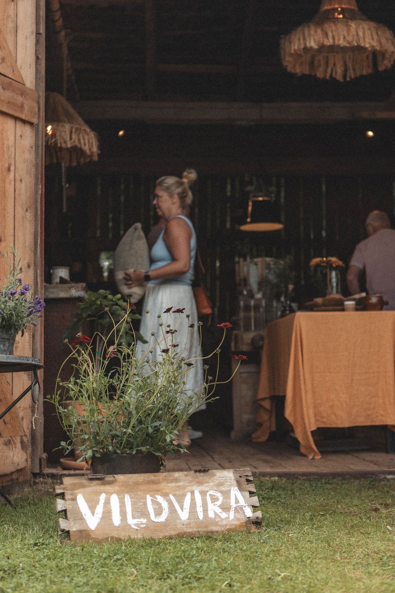 Rustic outdoor event space with wooden Vildvira sign and potted wildflowers.
