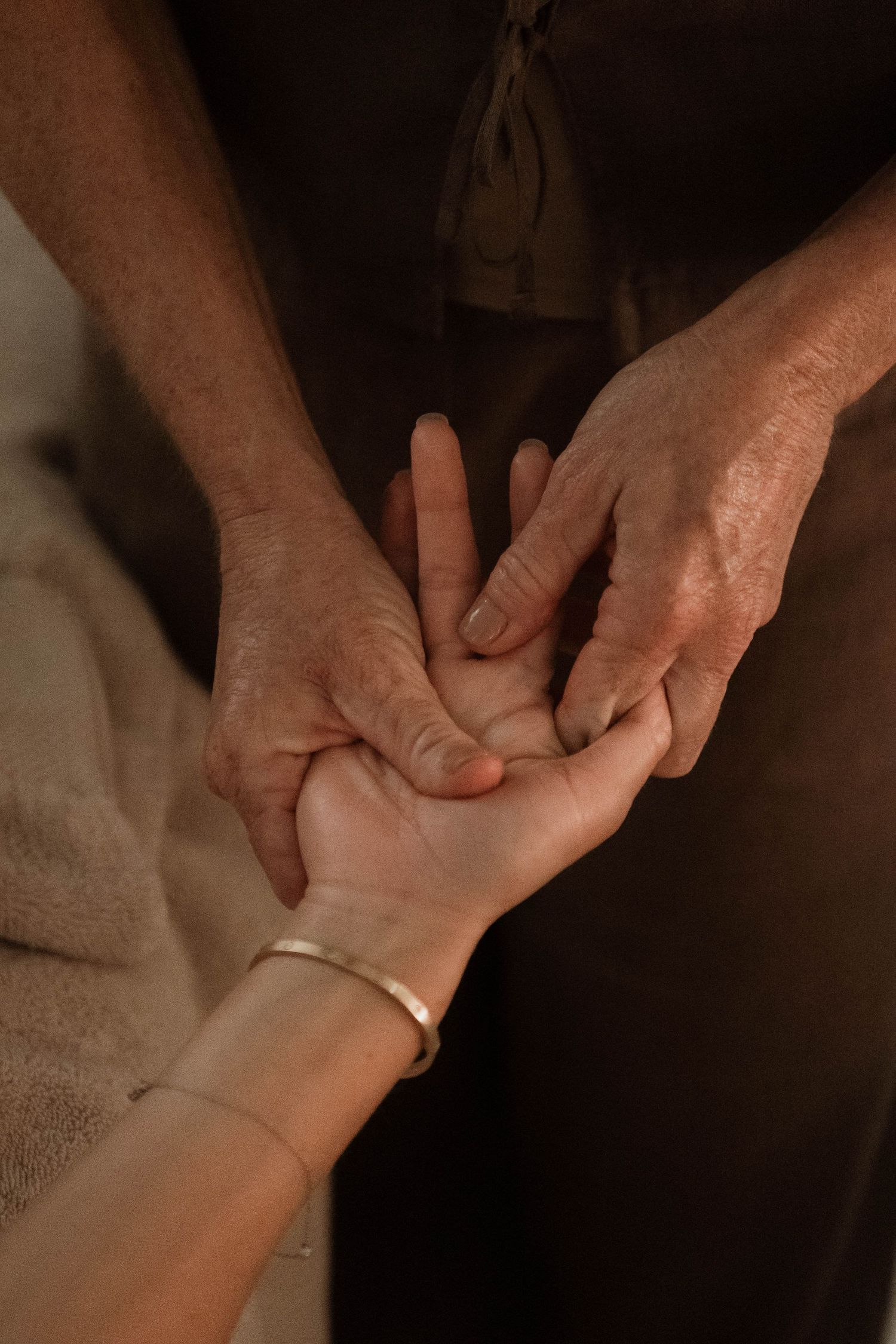 Close-up of hands performing palm massage therapy with bracelet detail in dim lighting.