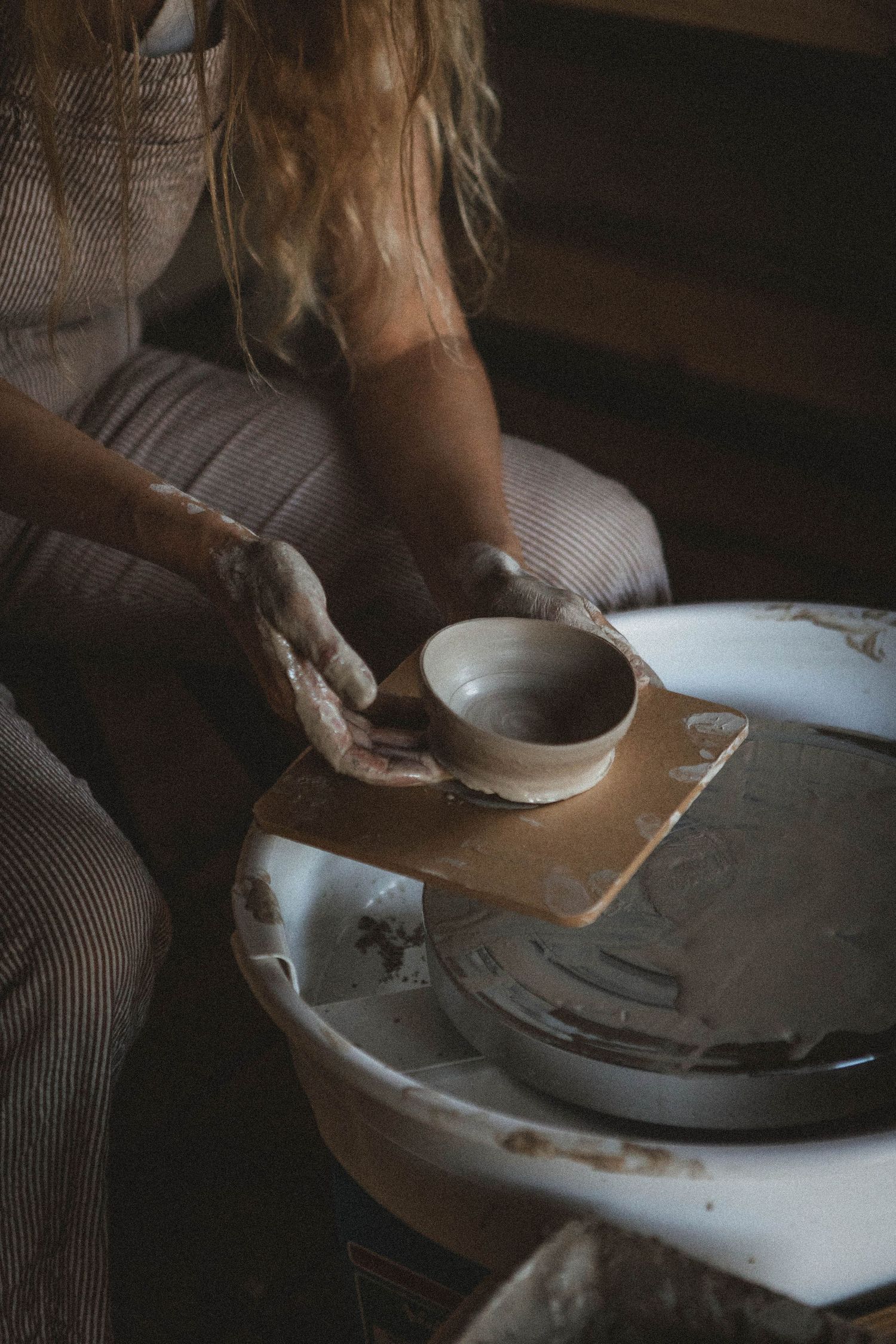 Close-up of hands shaping a small clay bowl on pottery wheel in rustic setting.