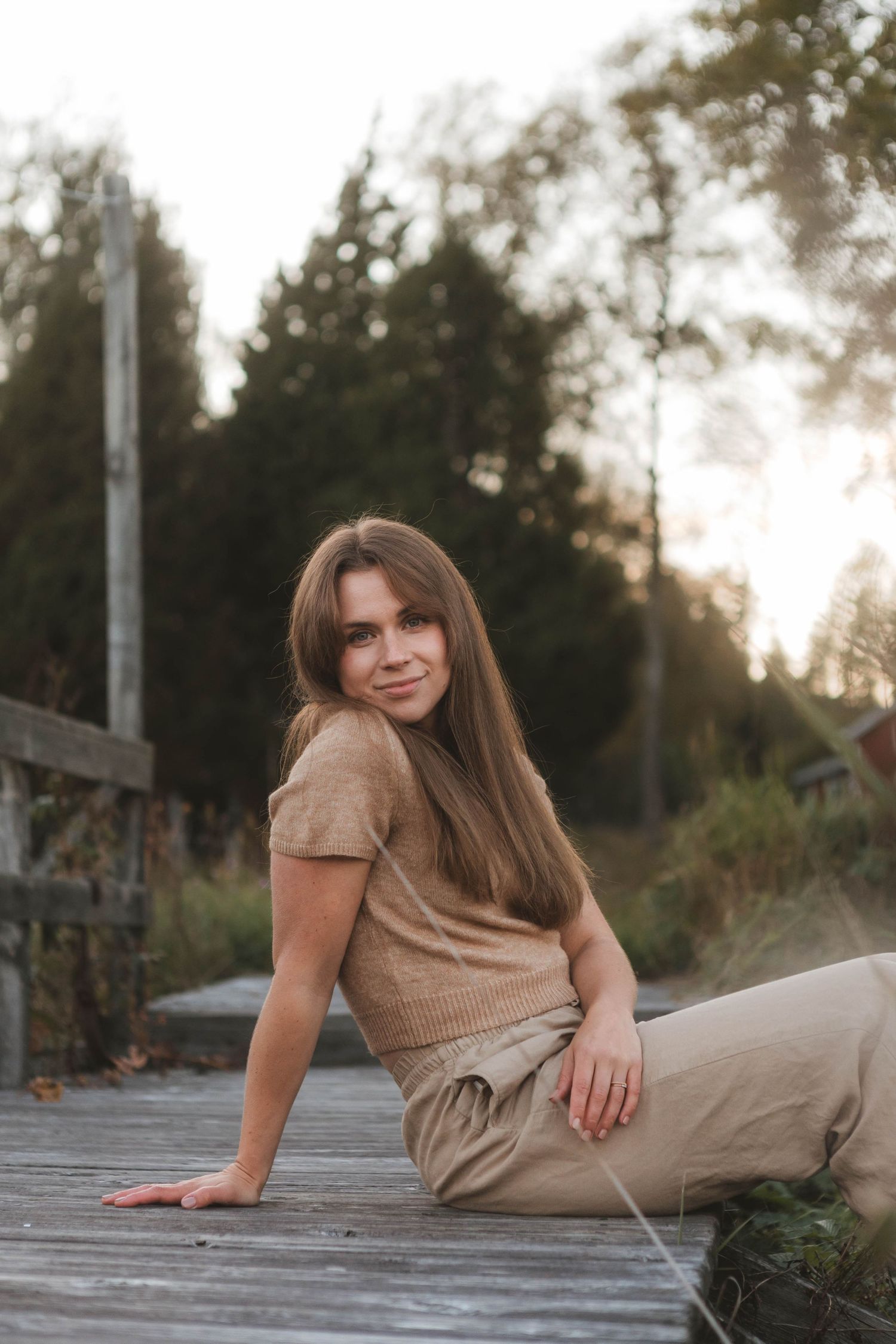 Someone in casual beige attire sits on a wooden deck during golden hour sunset in a natural outdoor setting.