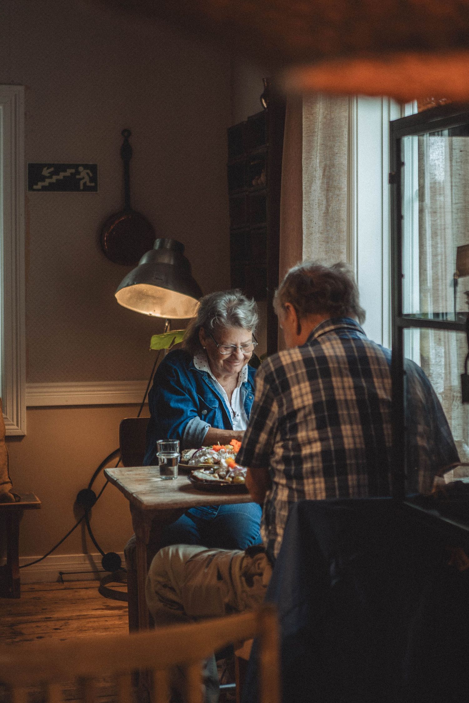 Cozy cafe scene with warm lamp lighting as patrons enjoy a meal at a window table.