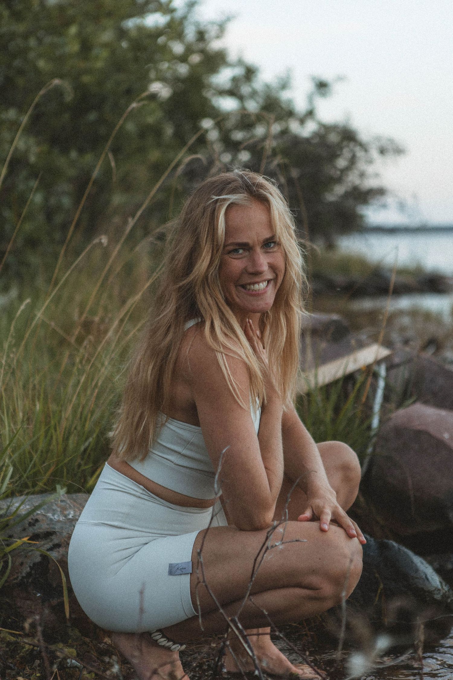 Person in white workout set sits on coastal rocks during golden hour.