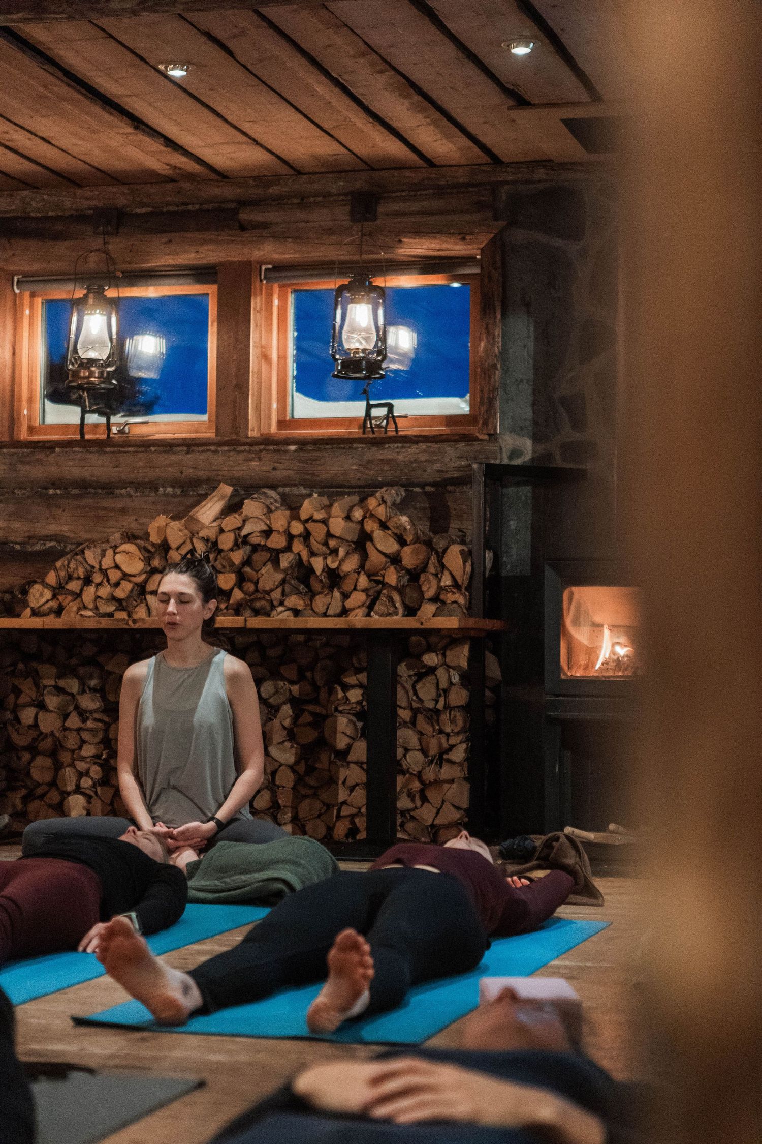 A meditation class taking place in a rustic cabin with oil lamps and stacked firewood creating a cozy atmosphere.