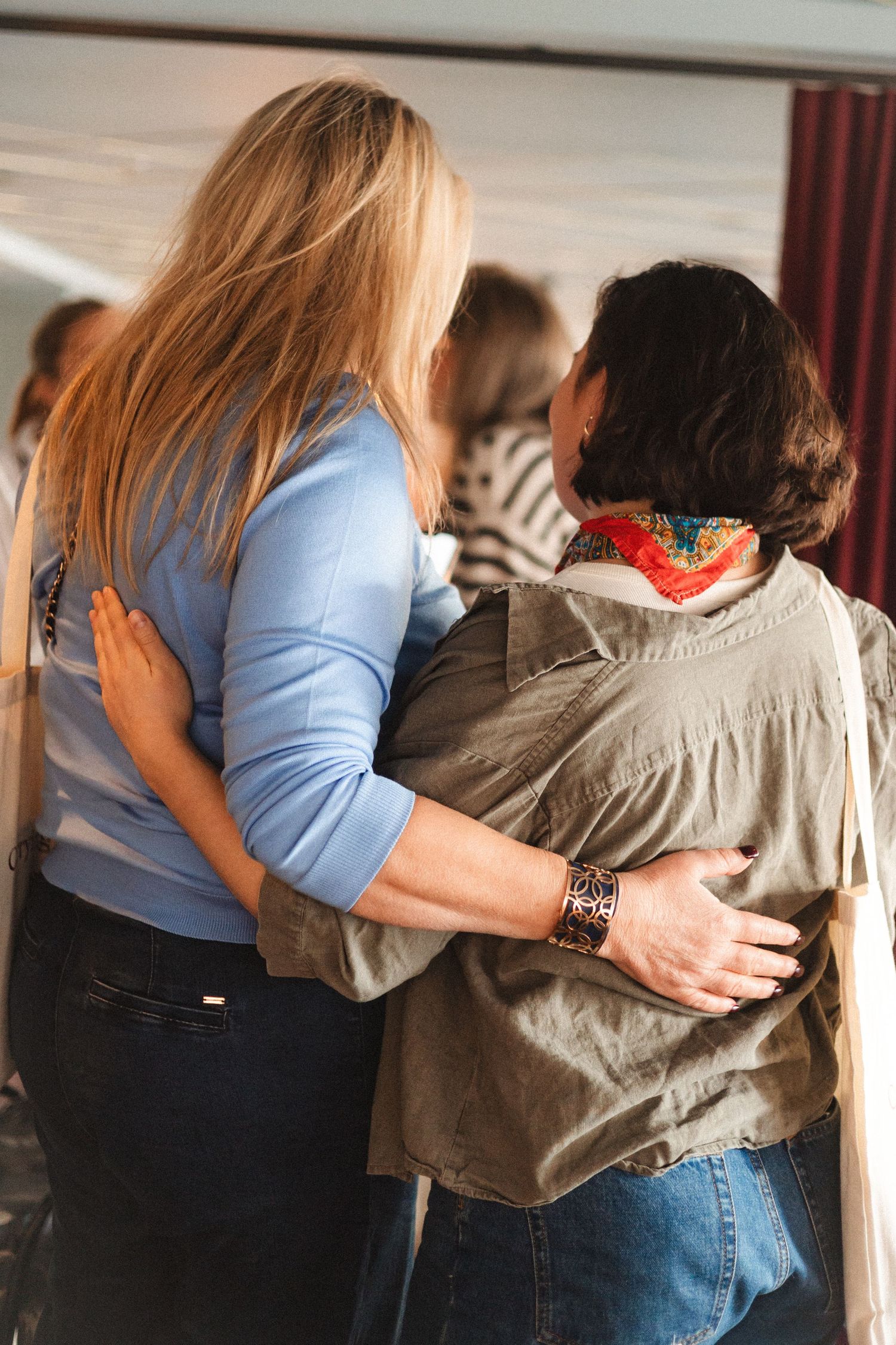 Two people embrace in a supportive gesture while standing in an indoor space.