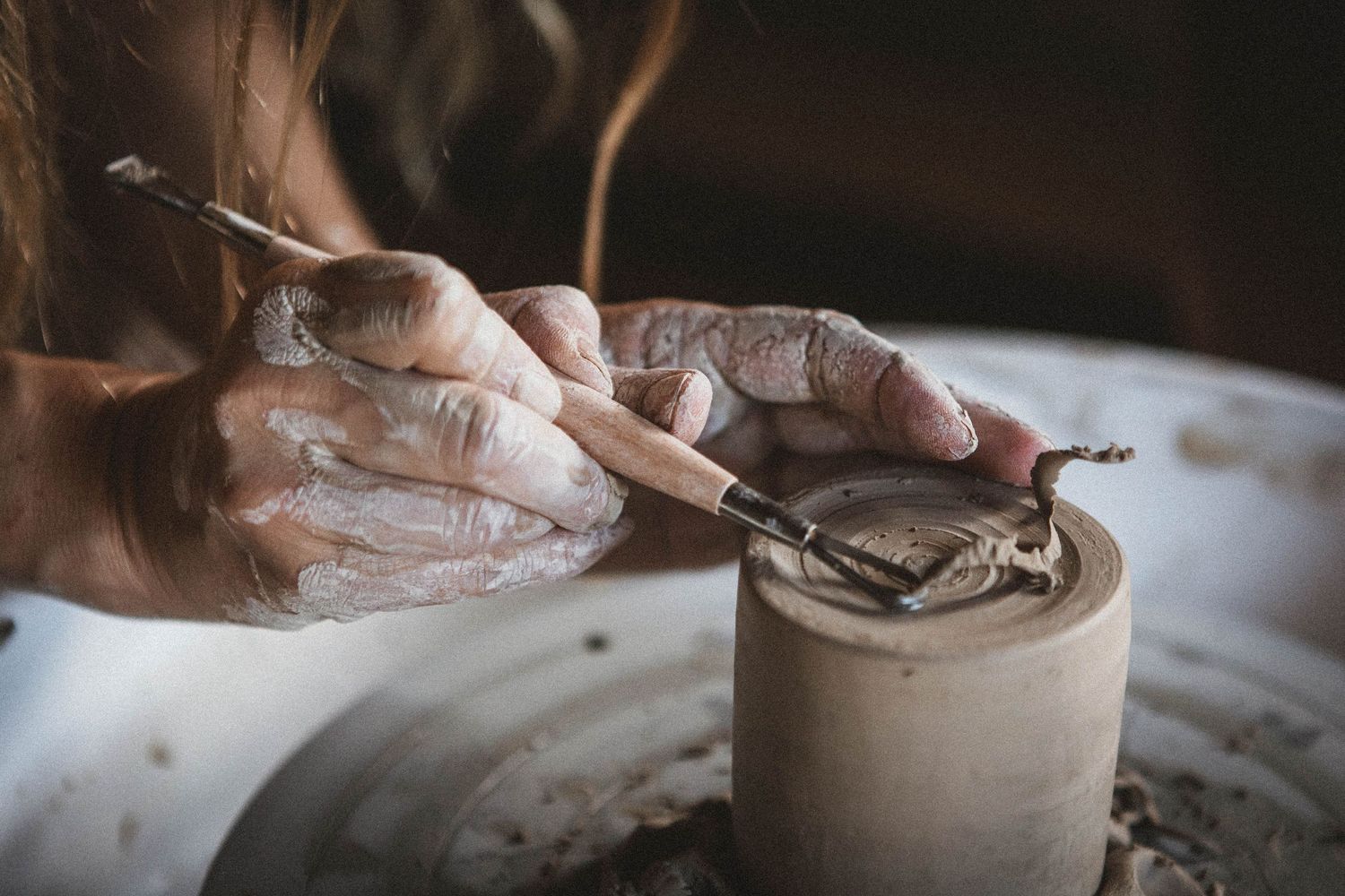 Hands carefully shaping and smoothing edges of small clay vessel on pottery wheel.