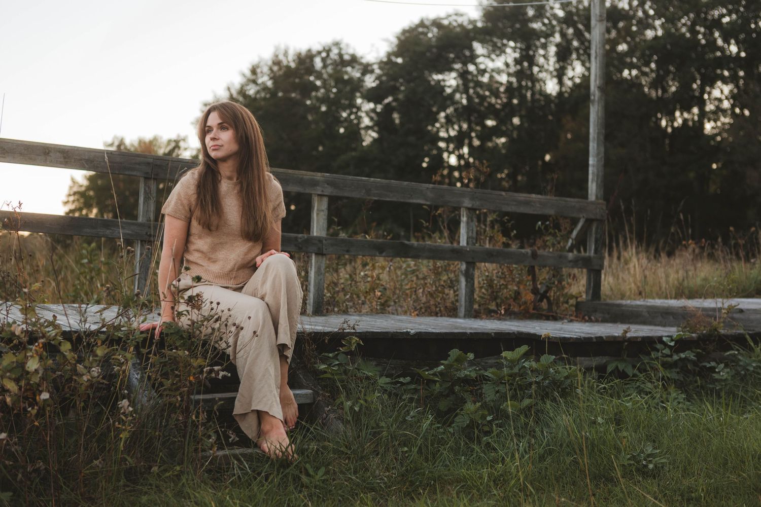 A person in a flowing white dress poses gracefully on a wooden bridge during golden hour.