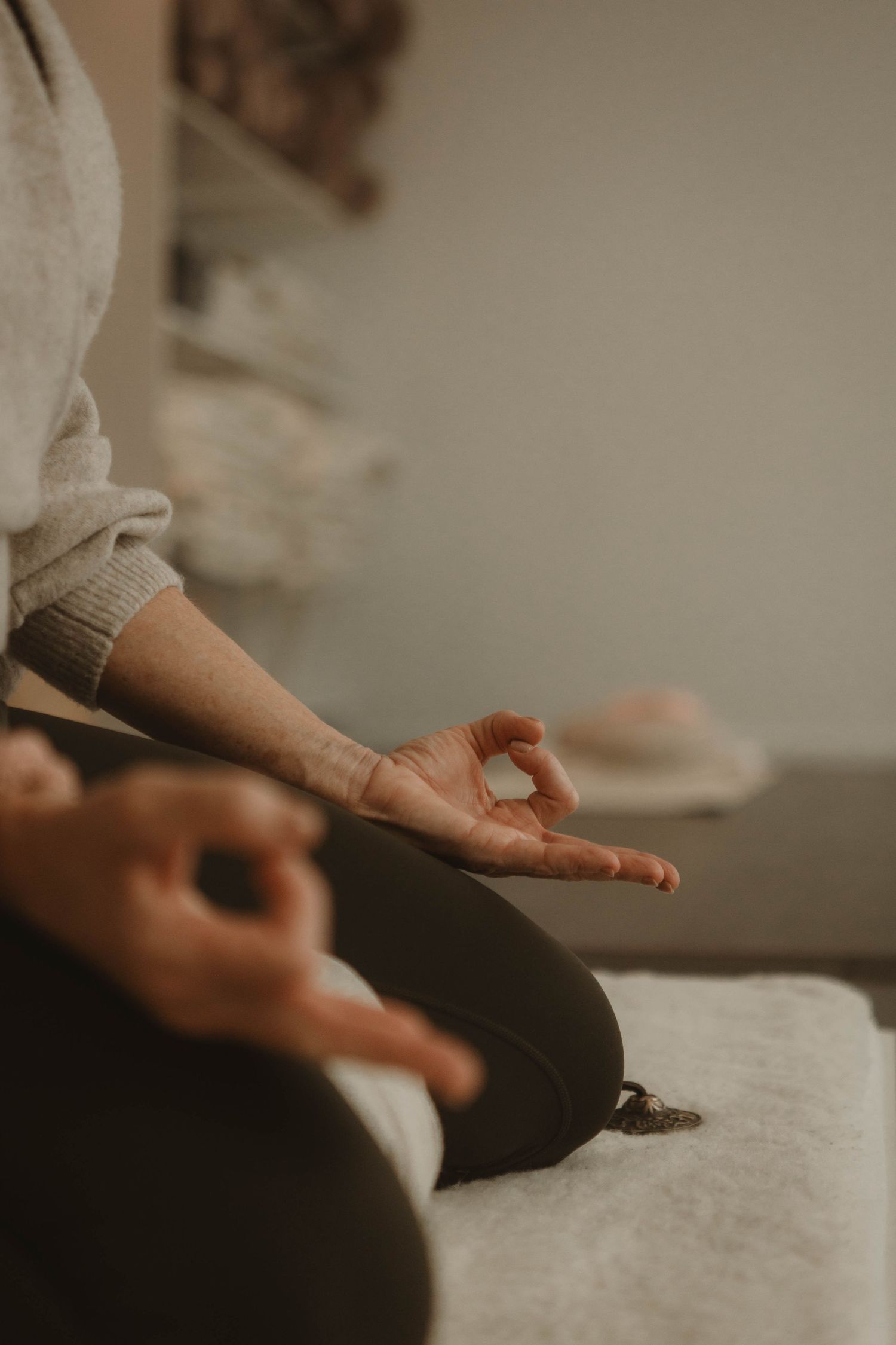 Person sits in meditation pose with hands in mudra position on white surface in warm lighting.