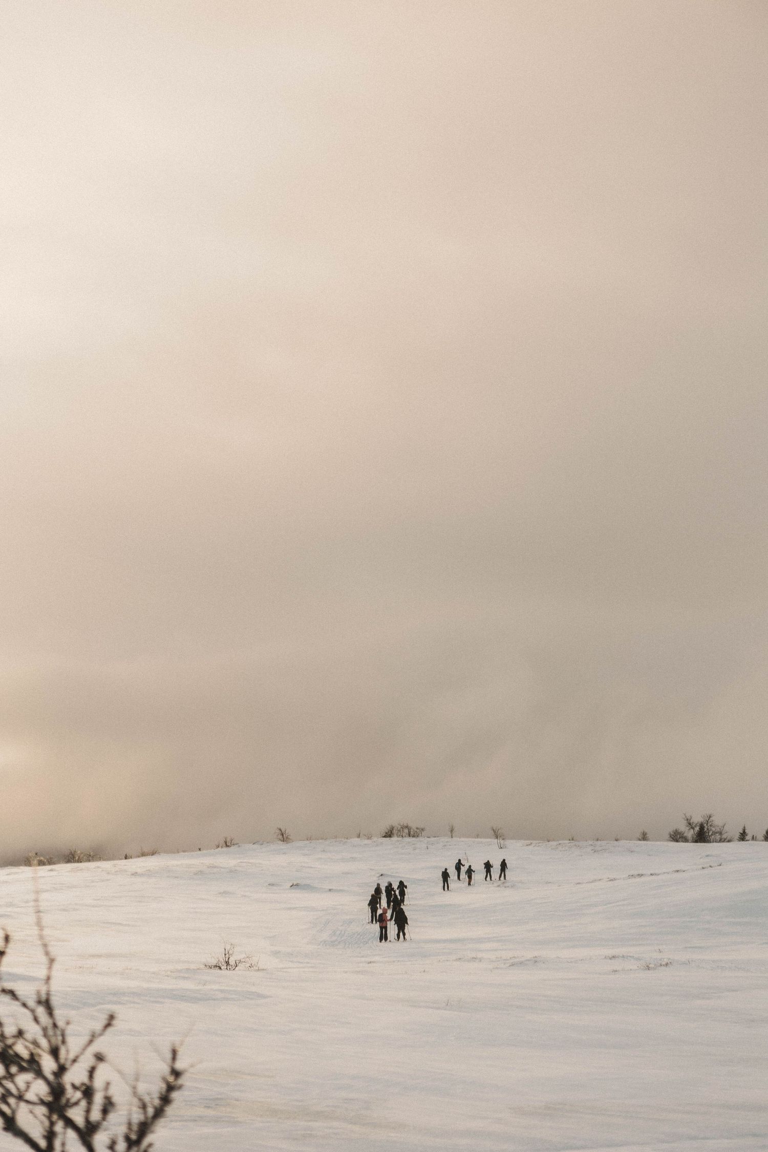 A distant group of people hiking across a snow-covered hill under an overcast winter sky.