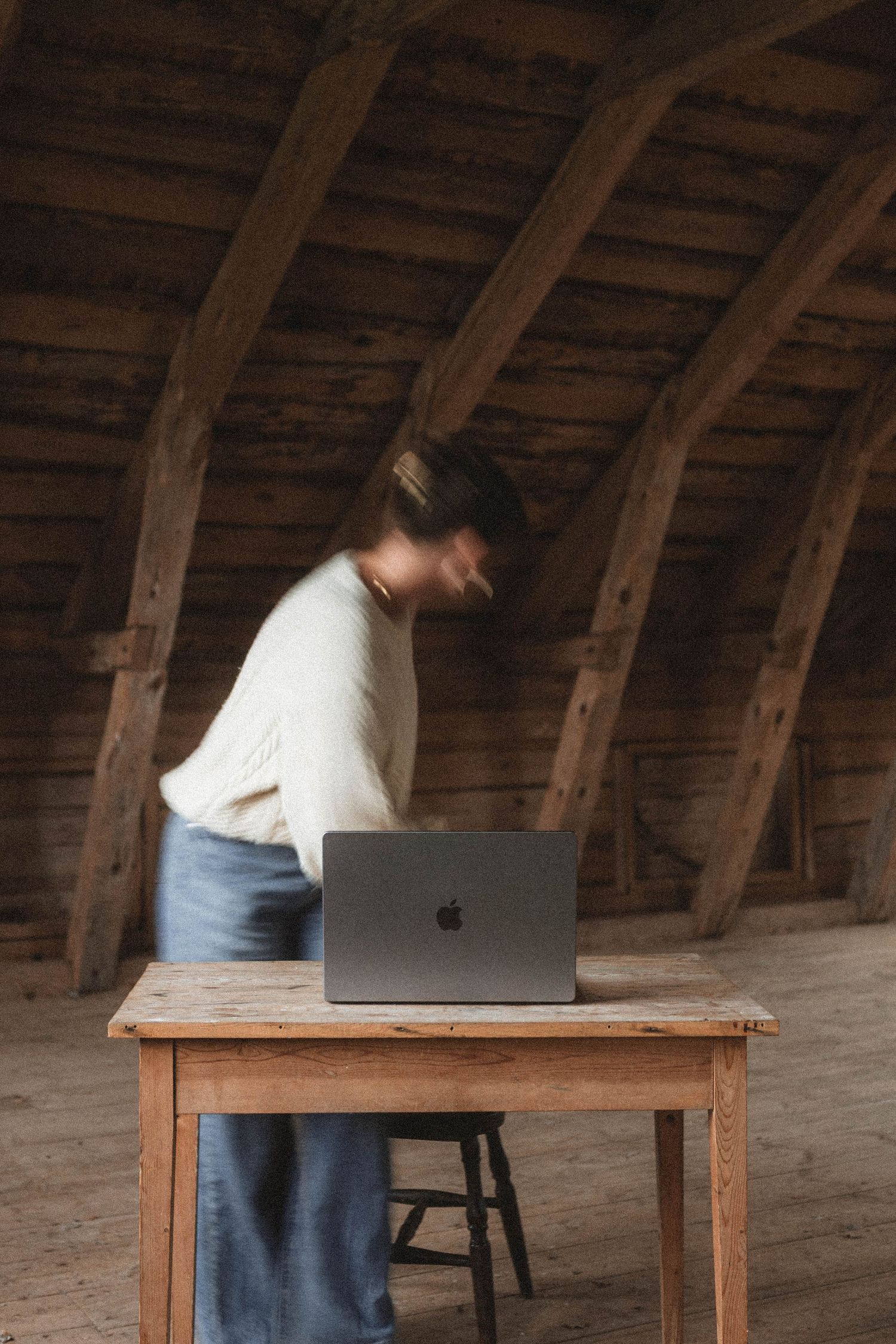 Minimalist sequence showing a person in casual attire working at a wooden desk in an attic space.