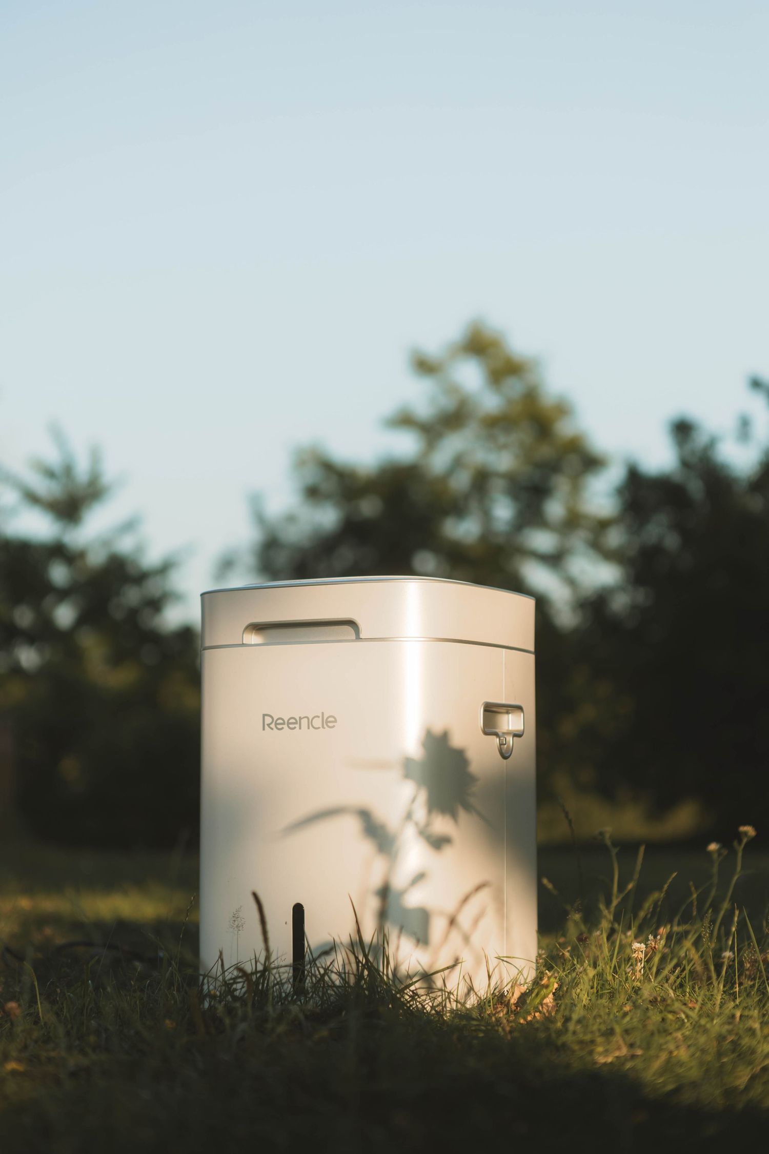 Three minimalist white cylindrical containers sit in grass at golden hour with soft natural lighting.