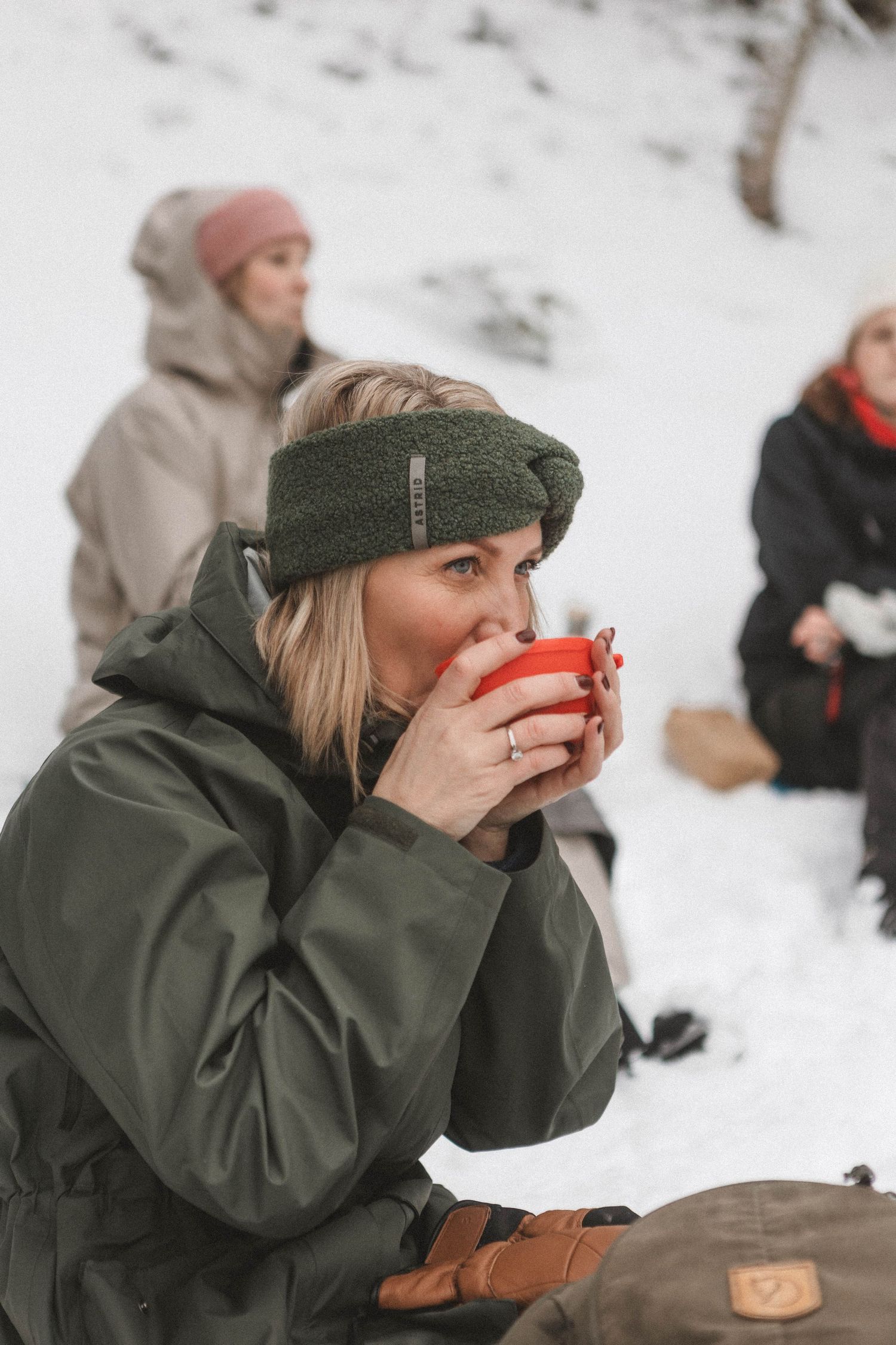 Someone sips from a red mug while wearing winter clothing and enjoying outdoor snowy weather with friends.