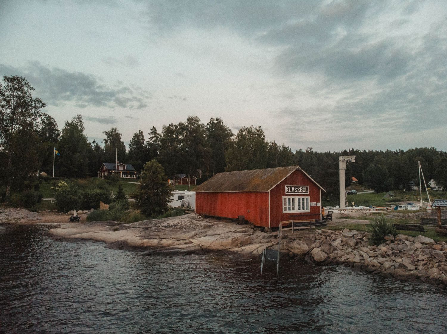 A red coastal cabin on rocky shores with water and forest in the background.